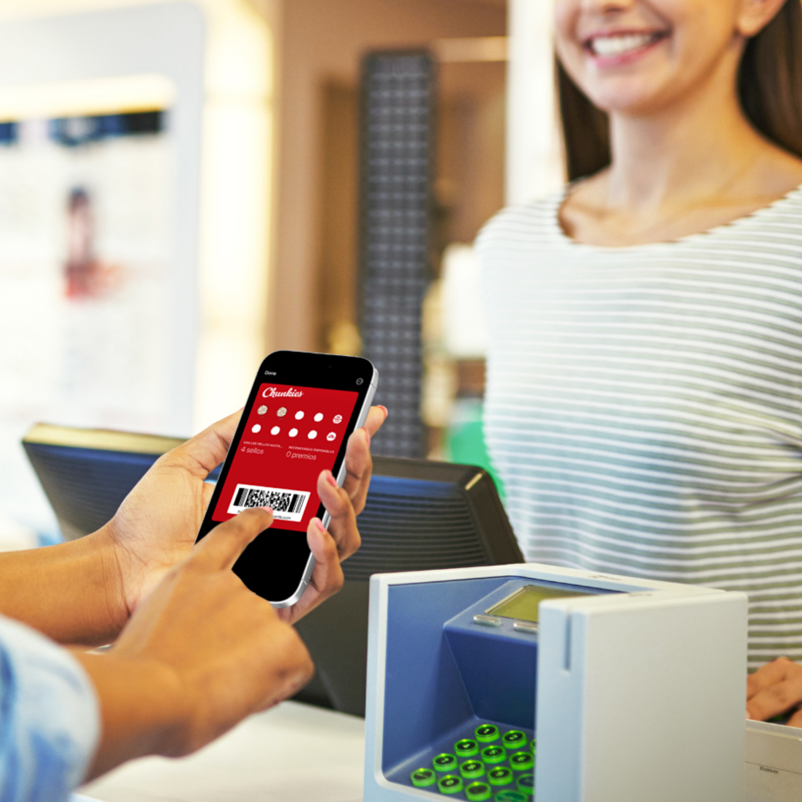 Una persona con uñas rosas sosteniendo un teléfono móvil en la caja registradora de una tienda, mostrando la pantalla de una aplicación de lotería, mientras otra persona, una mujer sonriente, espera en la caja.