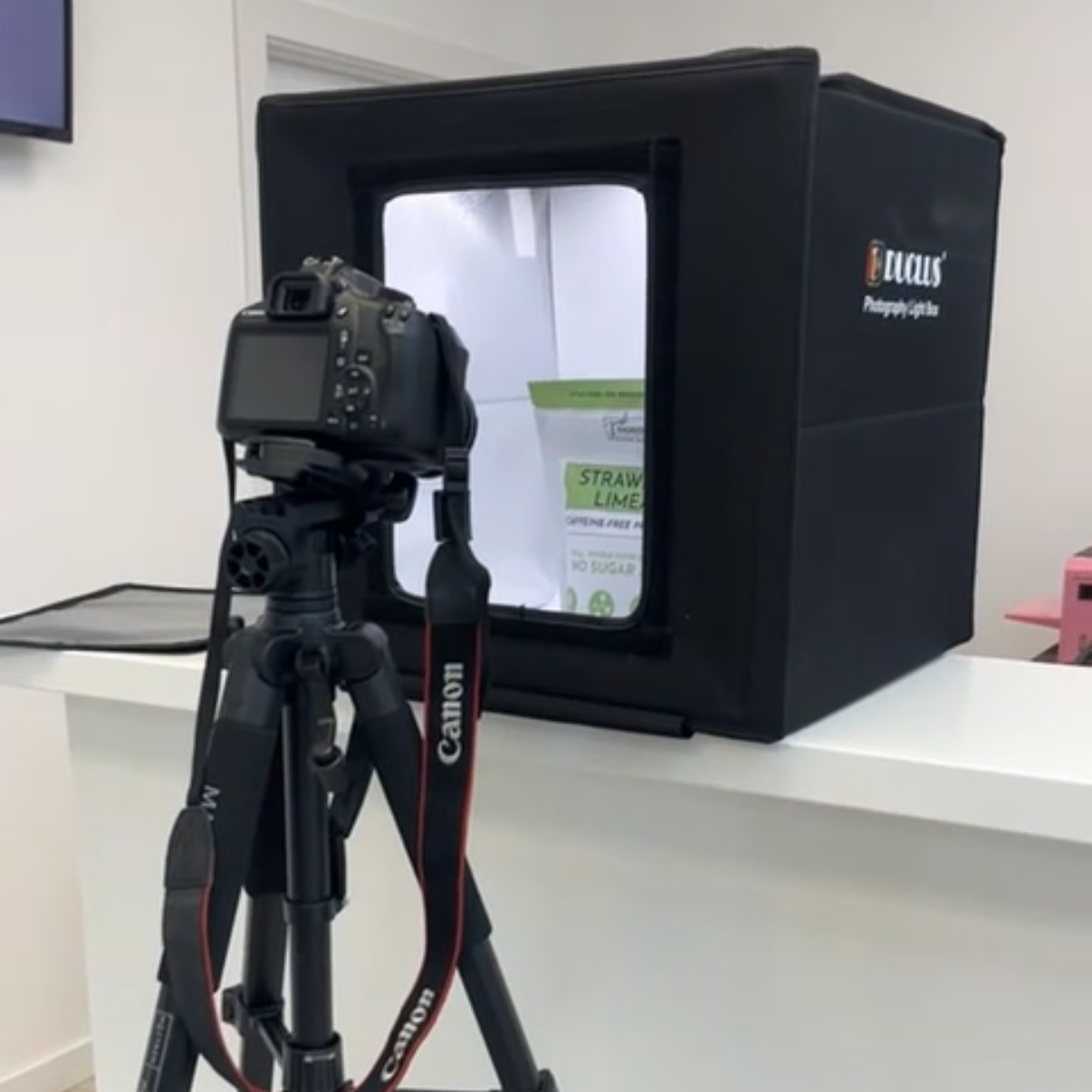 A camera on a tripod taking a photograph of a bag inside an illuminated lightbox.
