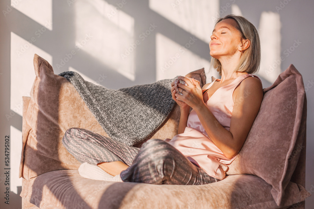 “Woman sitting in morning light with a warm drink, relaxing on a sofa and reflecting quietly.”