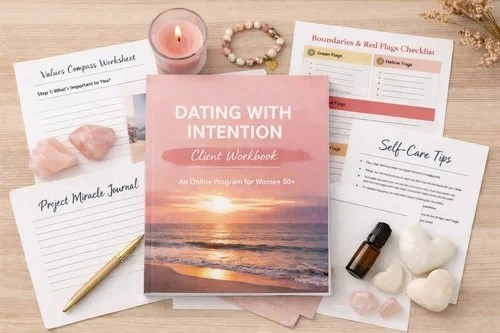 The Dating With Intention Client Workbook displayed on a wooden table with supportive tools including worksheets, a soft pink candle, a beaded bracelet, a pen, white stones, a plant, and a checklist, all arranged to evoke calm and clarity.