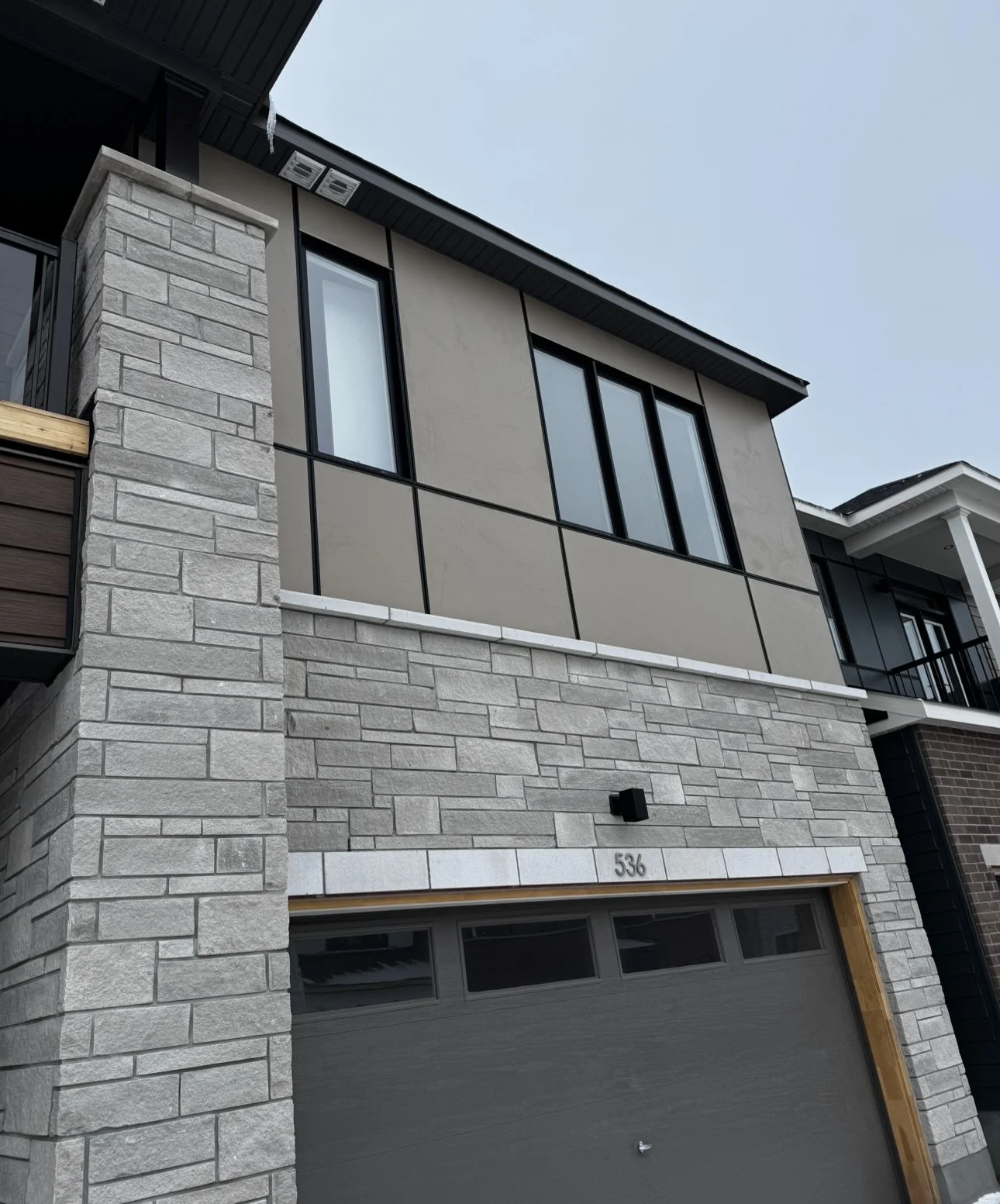Modern two-story house with gray stone brick and stucco exterior, black window frames, and a gray garage door, with the house number 536 above the garage.