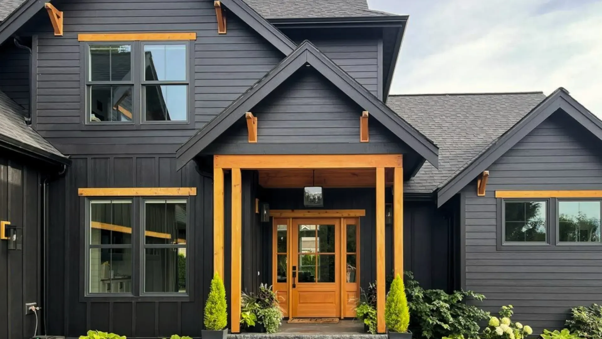 Black house with wooden accents and front porch, surrounded by plants and greenery.