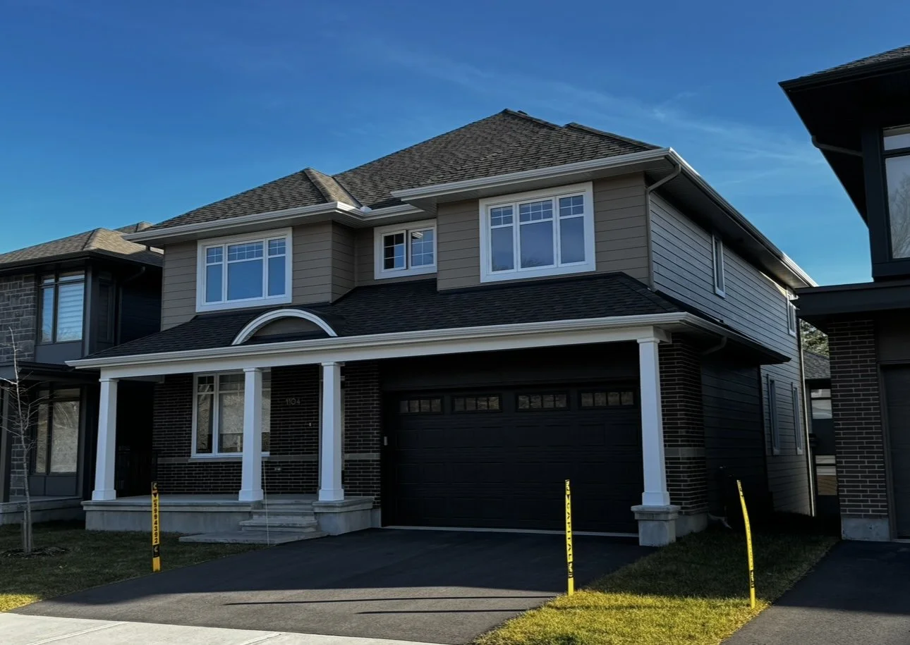 Modern two-story house with brick and beige siding, white trim, a black garage door, and a front porch with four white columns under a clear blue sky.