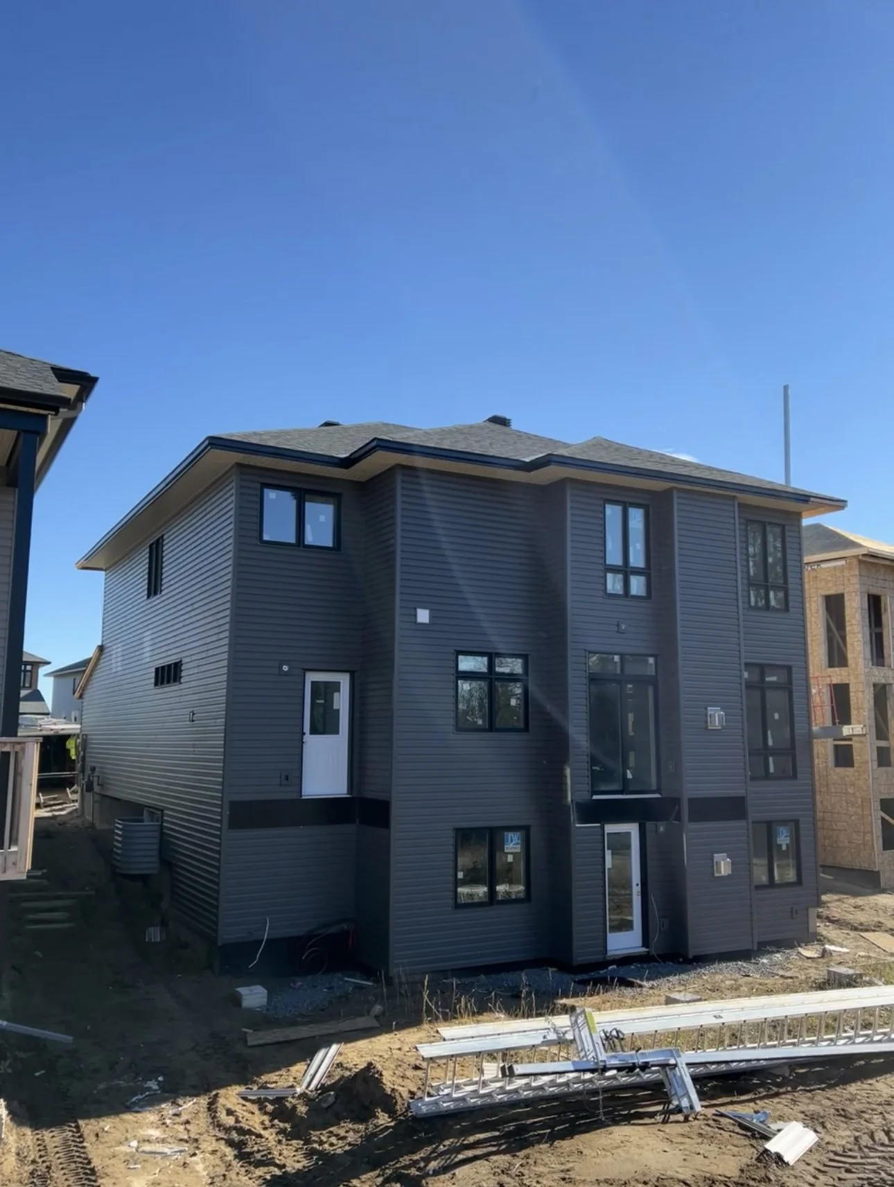 Newly built gray three-story house under construction with windows, side door, and construction materials in front.