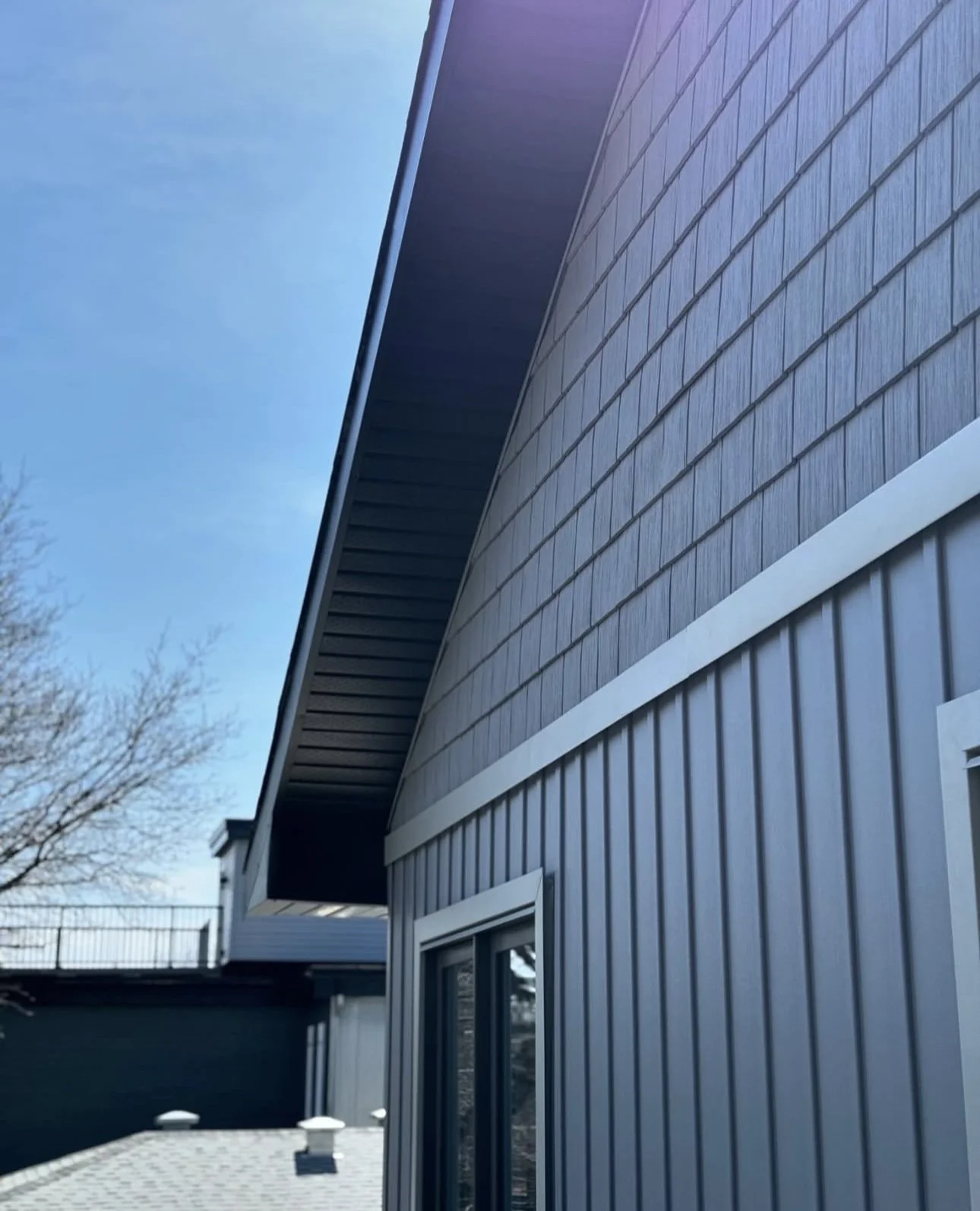 Close-up of a modern house exterior with blue siding, white trim, and a roof overhang against a clear blue sky.