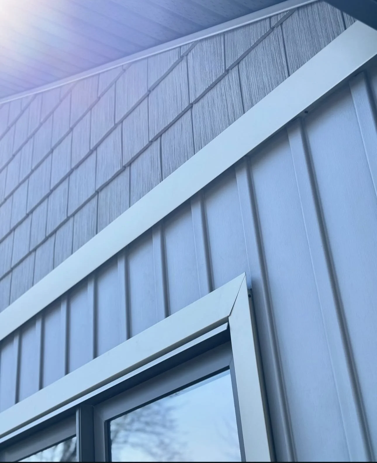 Close-up view of a house exterior showing blue siding, blue metal wall panels, and a white corner trim.