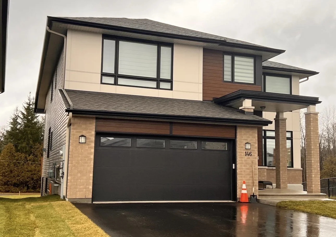 Modern two-story house with brick and siding exterior, black garage door, and covered front porch, on overcast day.