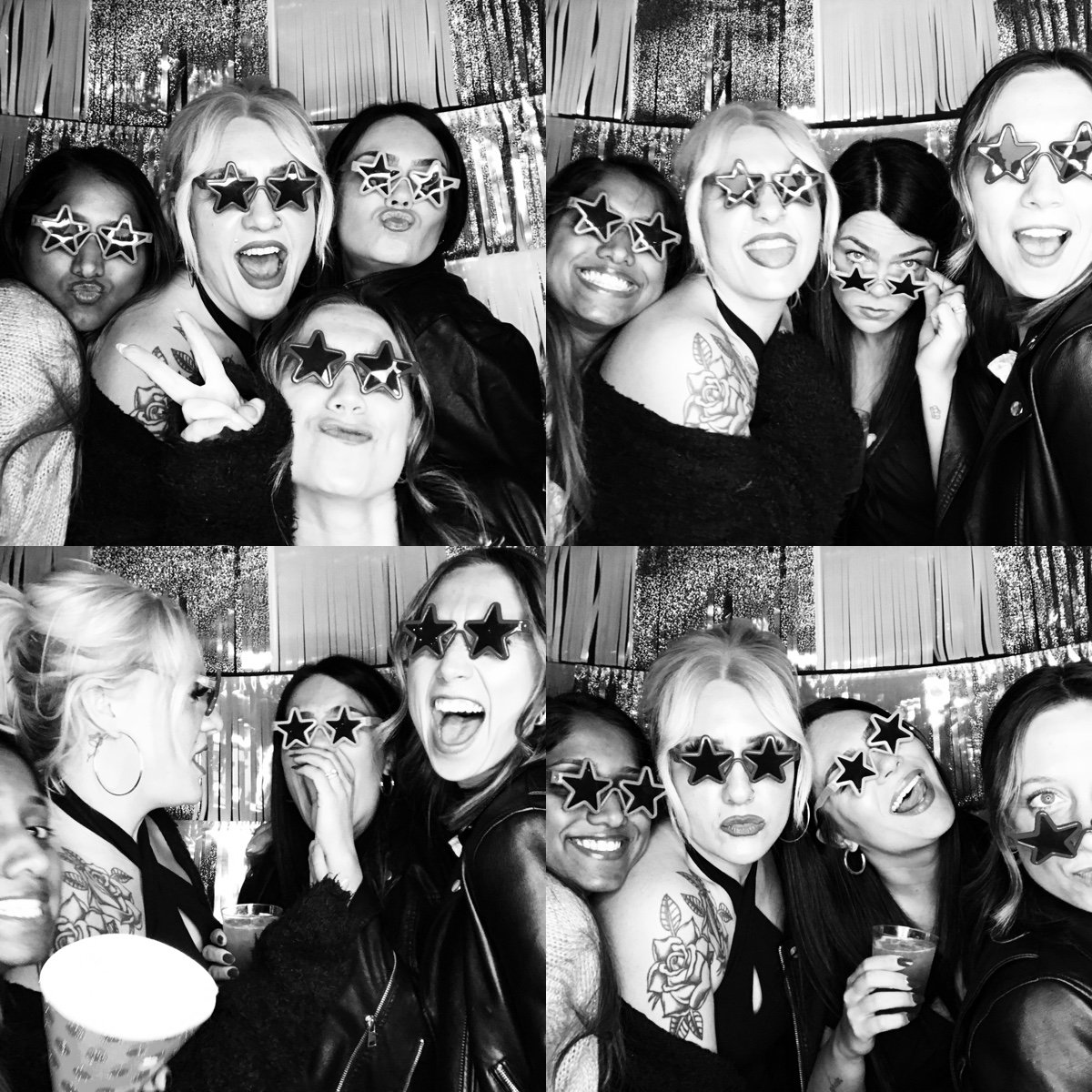 Group of women at a party wearing star-shaped sunglasses, posing for photos in a photo booth with sparkly background, dressed casually with tattoos and accessories, making joyful and playful expressions.