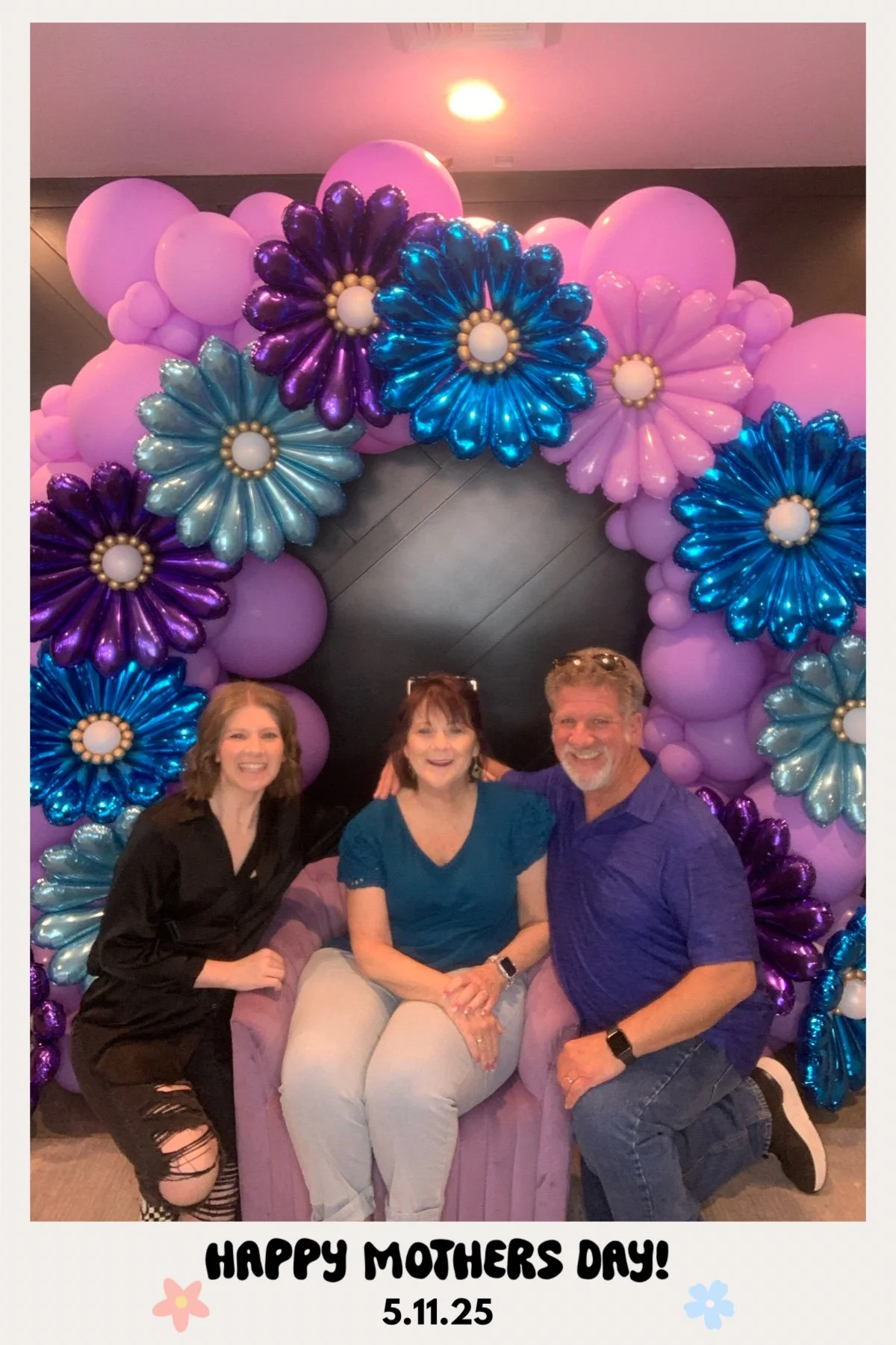 Three people sitting in front of a balloon floral arch celebrating Mother's Day, with the caption 'HAPPY MOTHER'S DAY! 5.11.25' at the bottom.