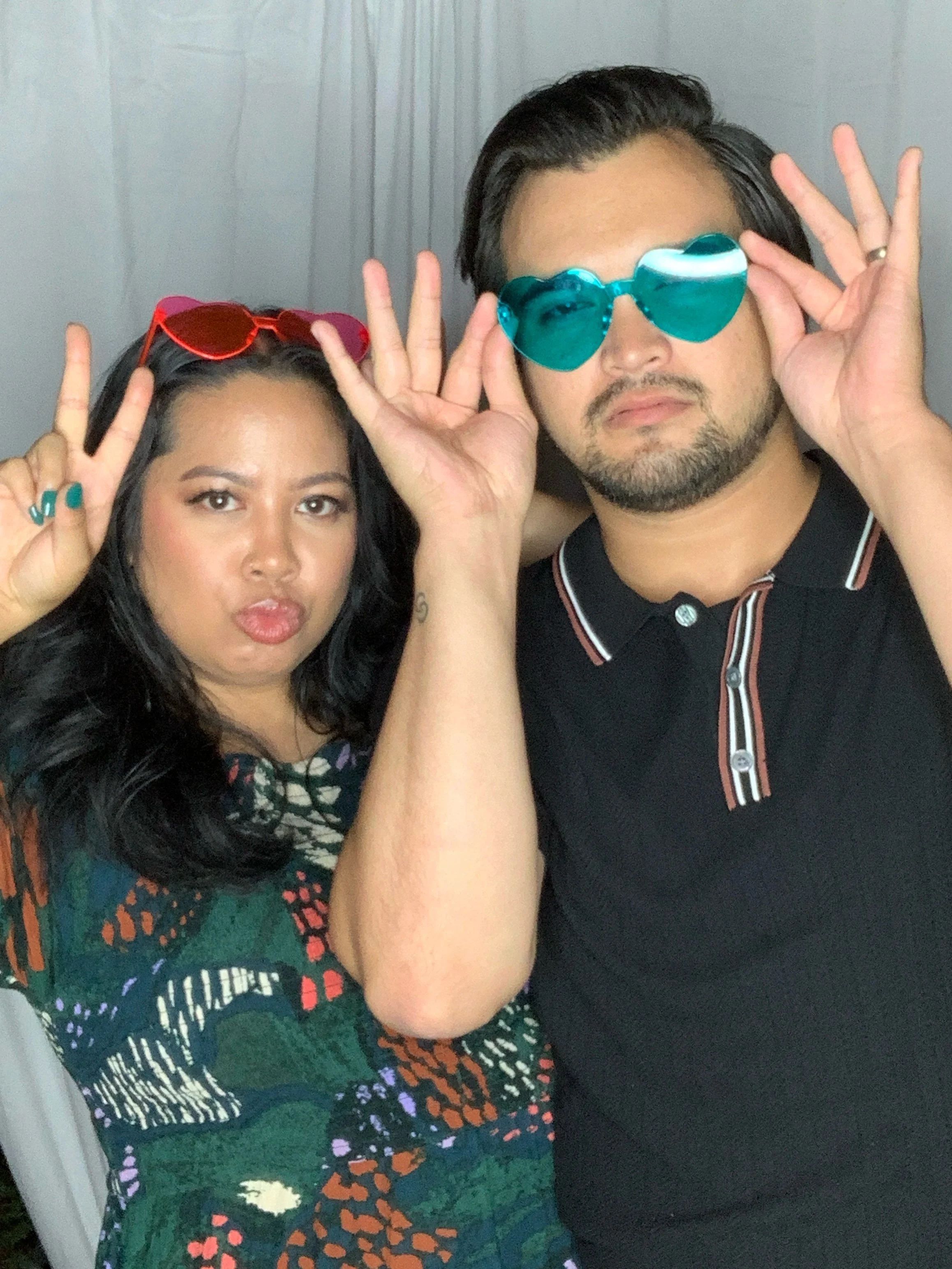 Two people wearing colorful sunglasses making playful expressions, posing together indoors.