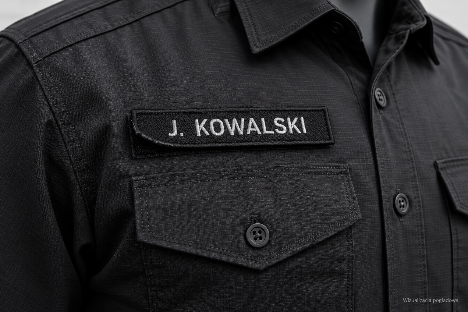 Haftowany imiennik J. KOWALSKI nad kieszenią czarnej koszuli mundurowej