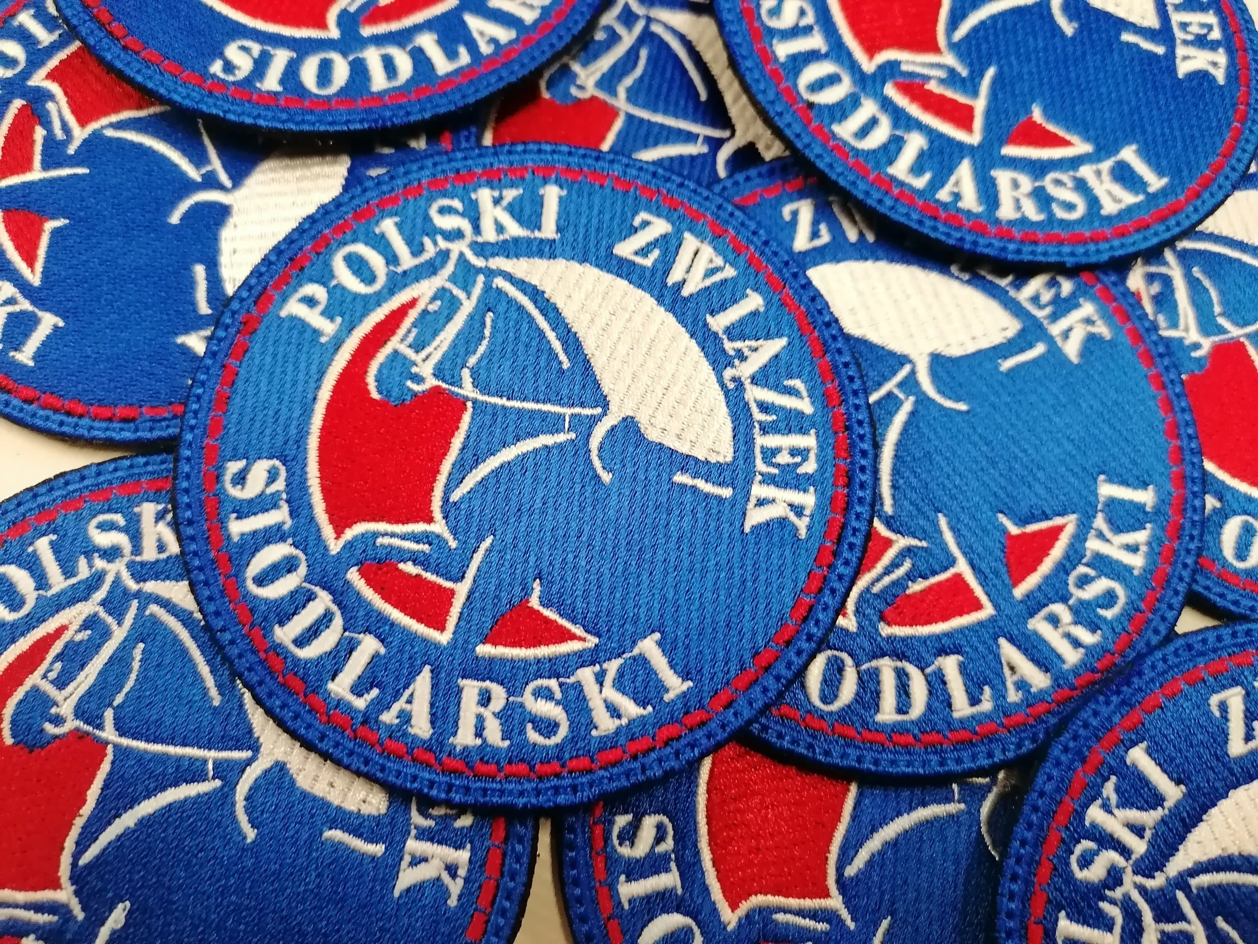 Niebieskie naszywki Polskiego Związku Siodlarskiego z głową konia i czerwono-białymi detalami
