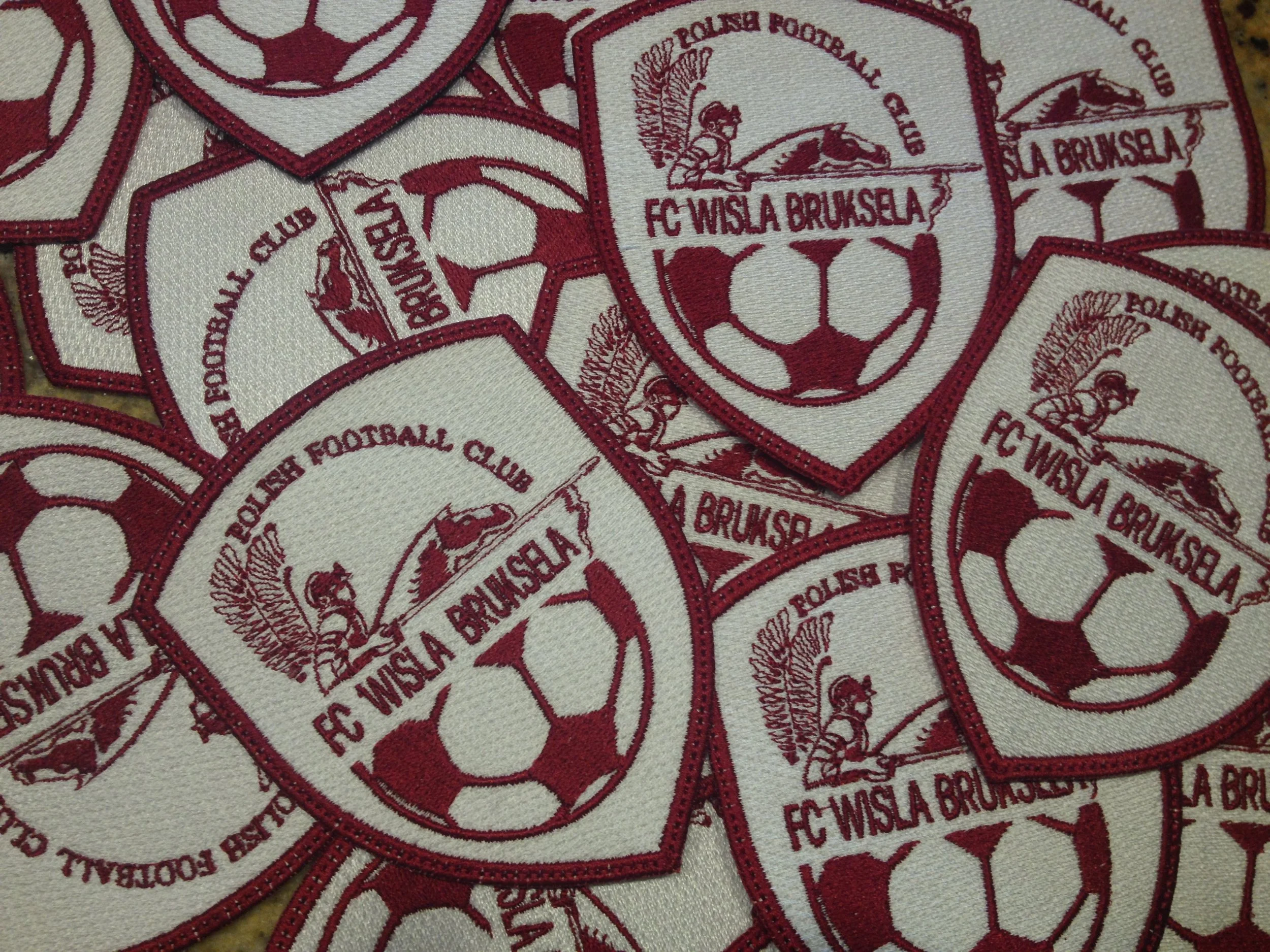 Biało-bordowe naszywki FC Wisła Bruksela w kształcie tarczy z piłką nożną i orłem