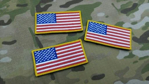 Trzy prostokątne haftowane flagi USA ułożone na maskującym materiale