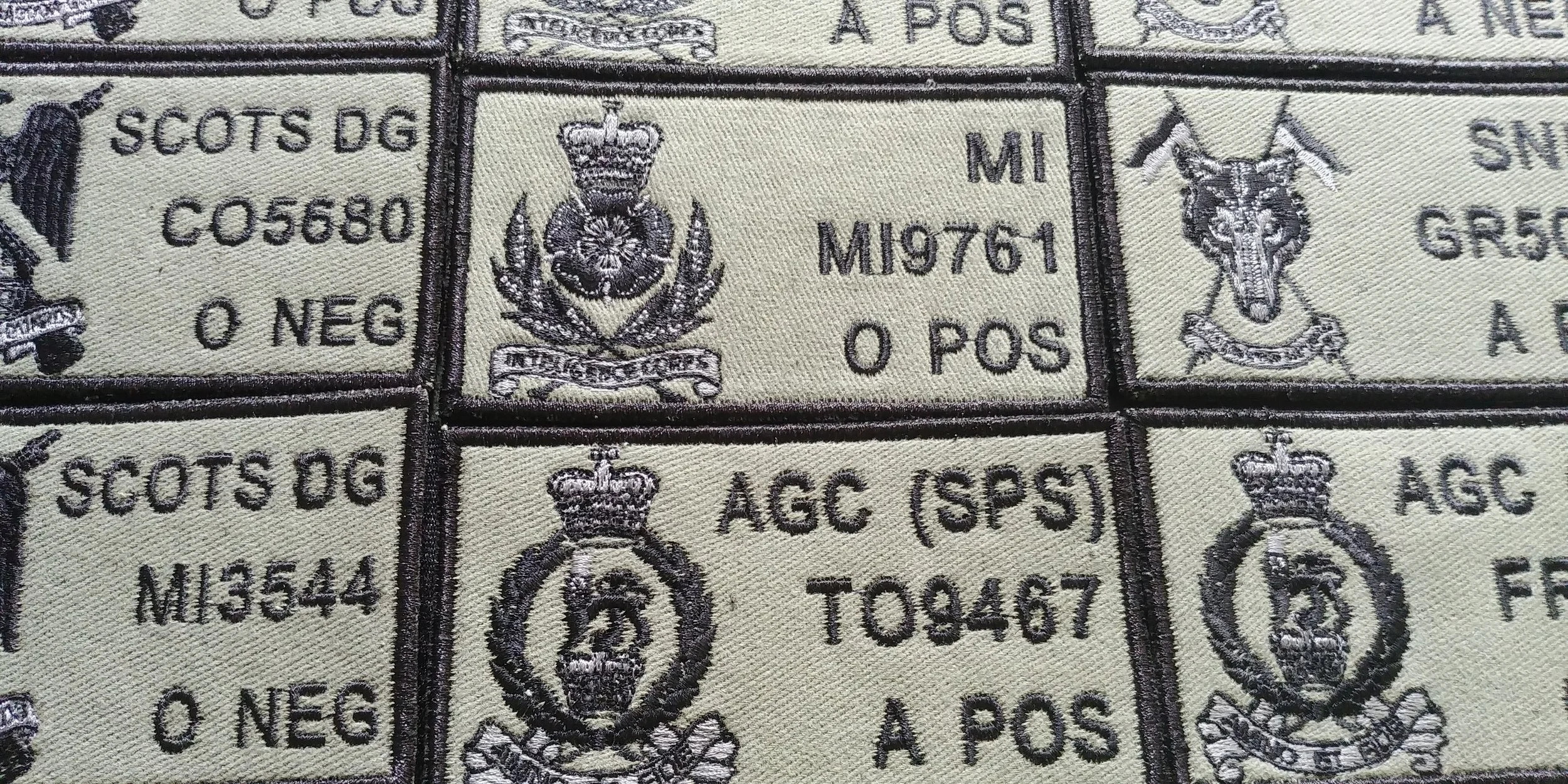 A close-up of embroidered patches with military insignia, including crowns, animals, and text such as 'SCOTS DG' and 'MI M9761'.