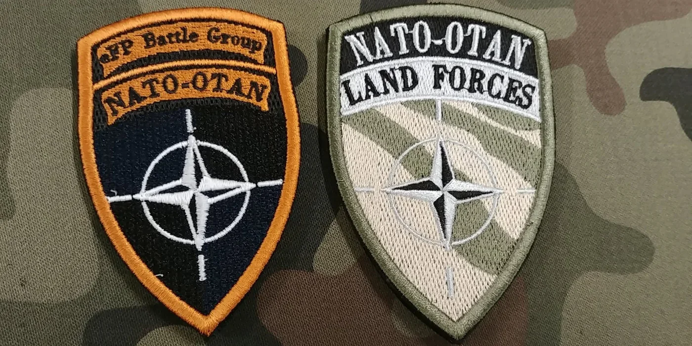 Porównanie dwóch haftowanych tarcz: eFP Battle Group NATO-OTAN z pomarańczowym obramowaniem oraz polowej NATO-OTAN Land Forces