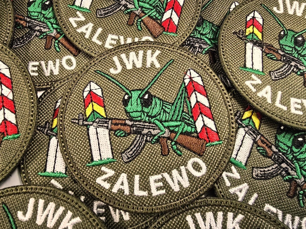 Oliwkowe naszywki haftowane JWK Zalewo z zielonym owadem trzymającym karabin i słupami granicznymi