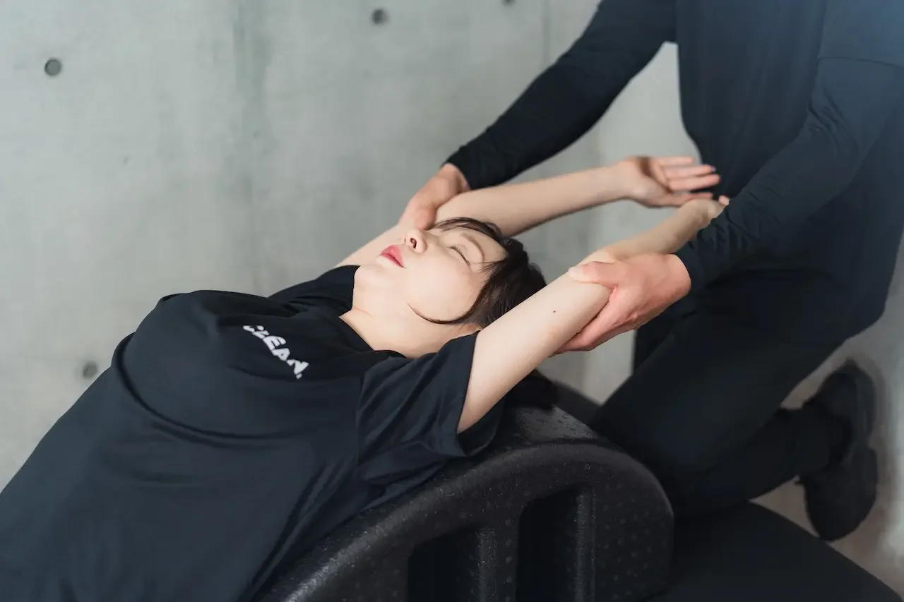 日吉のパーソナルジム「CLEAN.」にて、トレーニングのインターバル中に行われるパーソナルストレッチの様子。筋力トレーニングの合間にプロのトレーナーが可動域を広げる調整を行い、怪我の予防と効率的なボディメイクを両立させている。