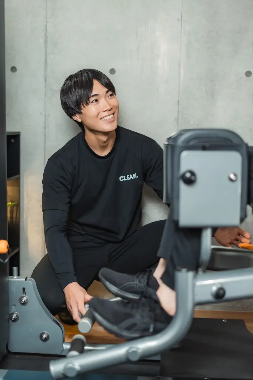 大手ジム全国1位の実績を持つ、日吉のパーソナルジム「CLEAN.」代表トレーナー・山際。清潔感のあるスタジオを背景に、誠実で親しみやすい笑顔で、一人ひとりに寄り添う本質改善を体現しているプロフィール写真。