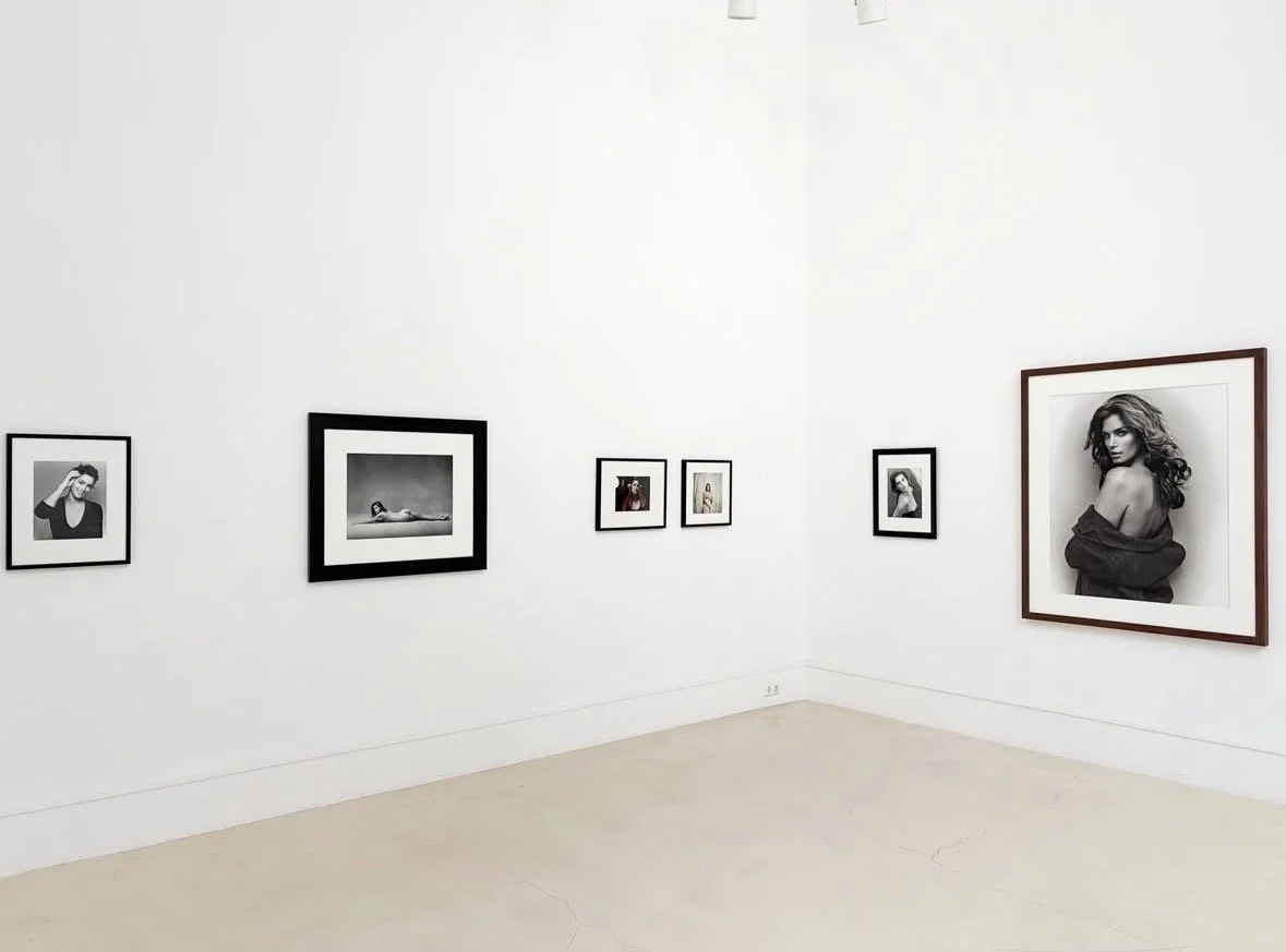 Gallery wall with black and white portrait photographs of women in various poses, framed and hung on white walls.