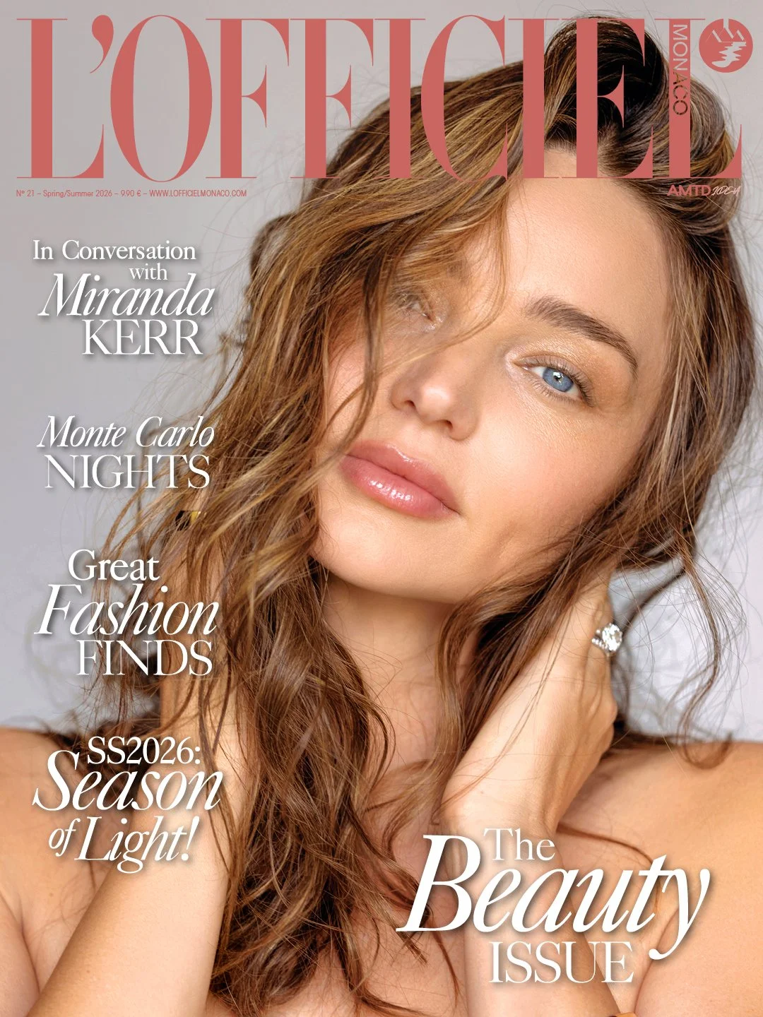 Close-up portrait of a young woman with wavy brown hair and blue eyes, gazing at the camera with a soft expression, wearing earrings and touching her hair.