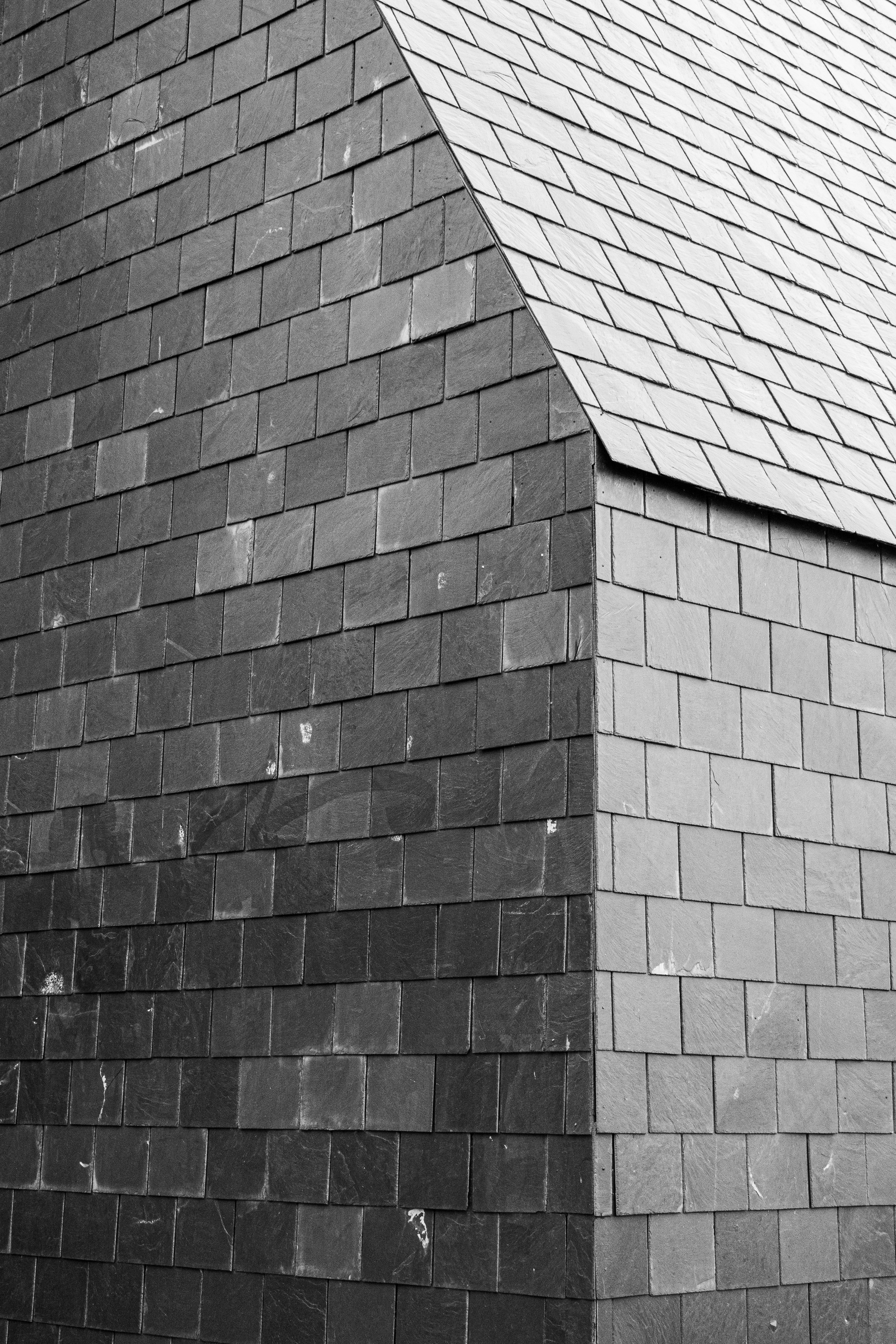 Close-up view of a corner of a building with brick and slate roofing shingles in black and white.