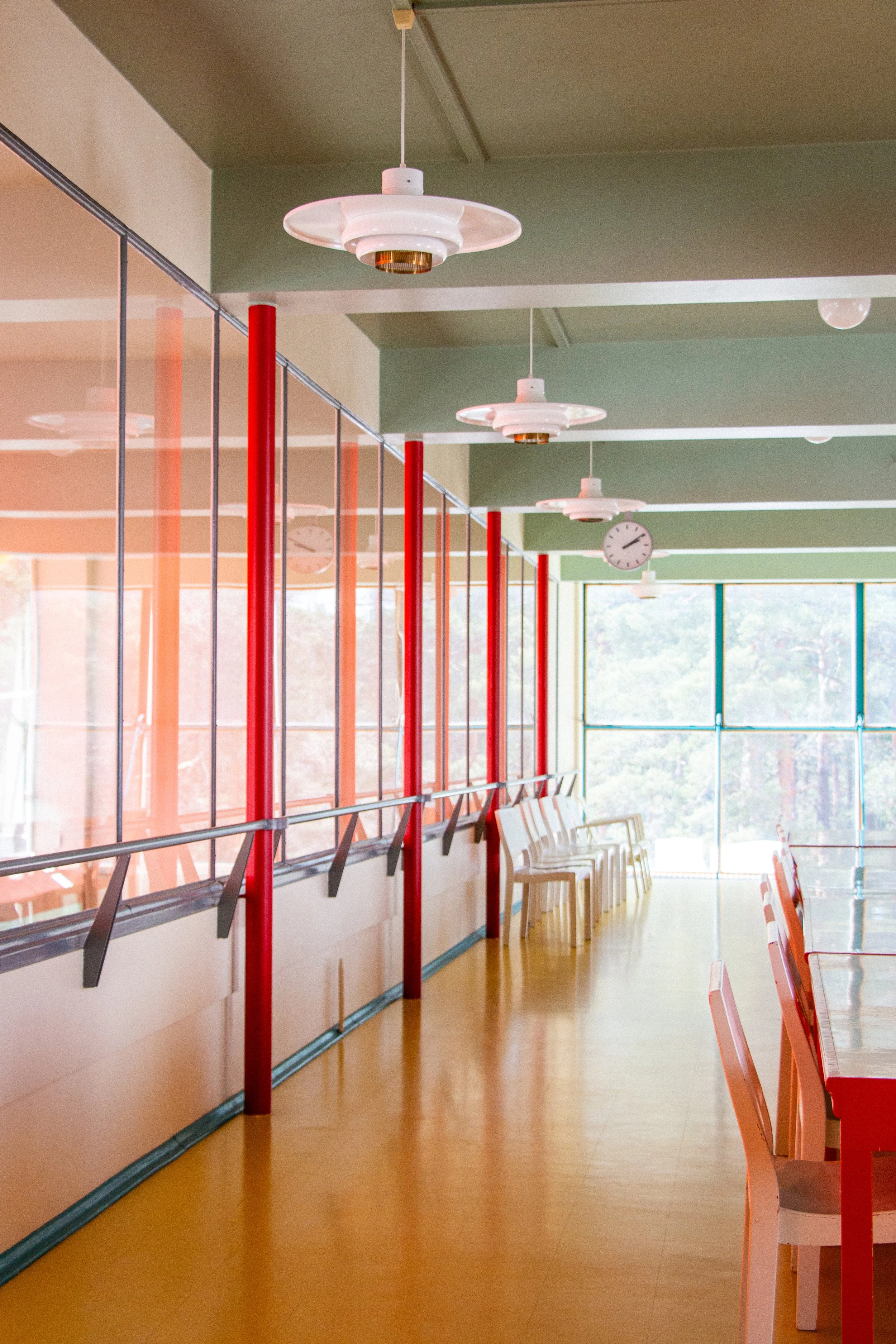 Empty indoor dining area with chairs, large windows, hanging ceiling lights, and a clock on the wall.