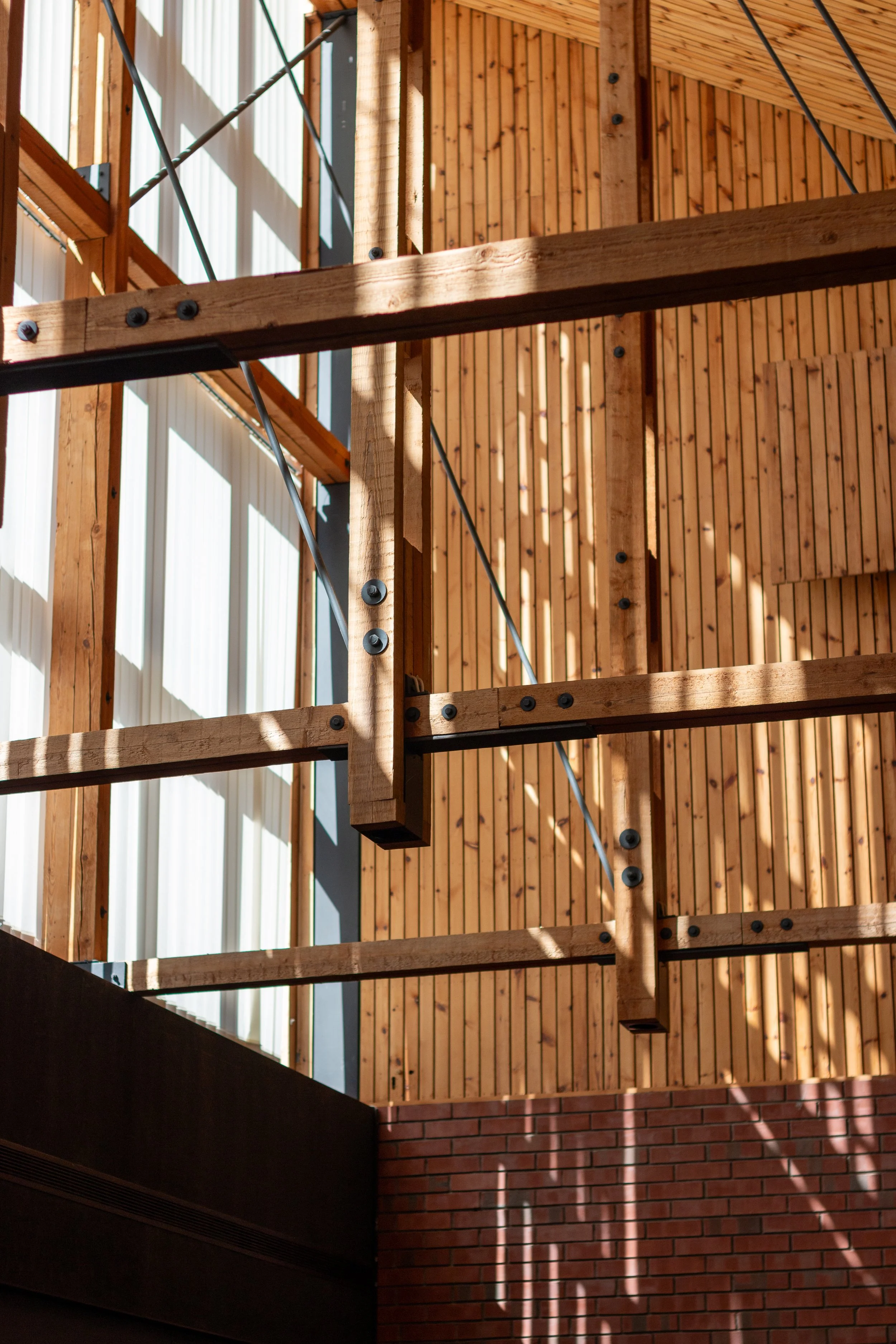 Interior of a building under construction with visible wooden beams, metal supports, and brick wall corner, sunlight casting shadows.