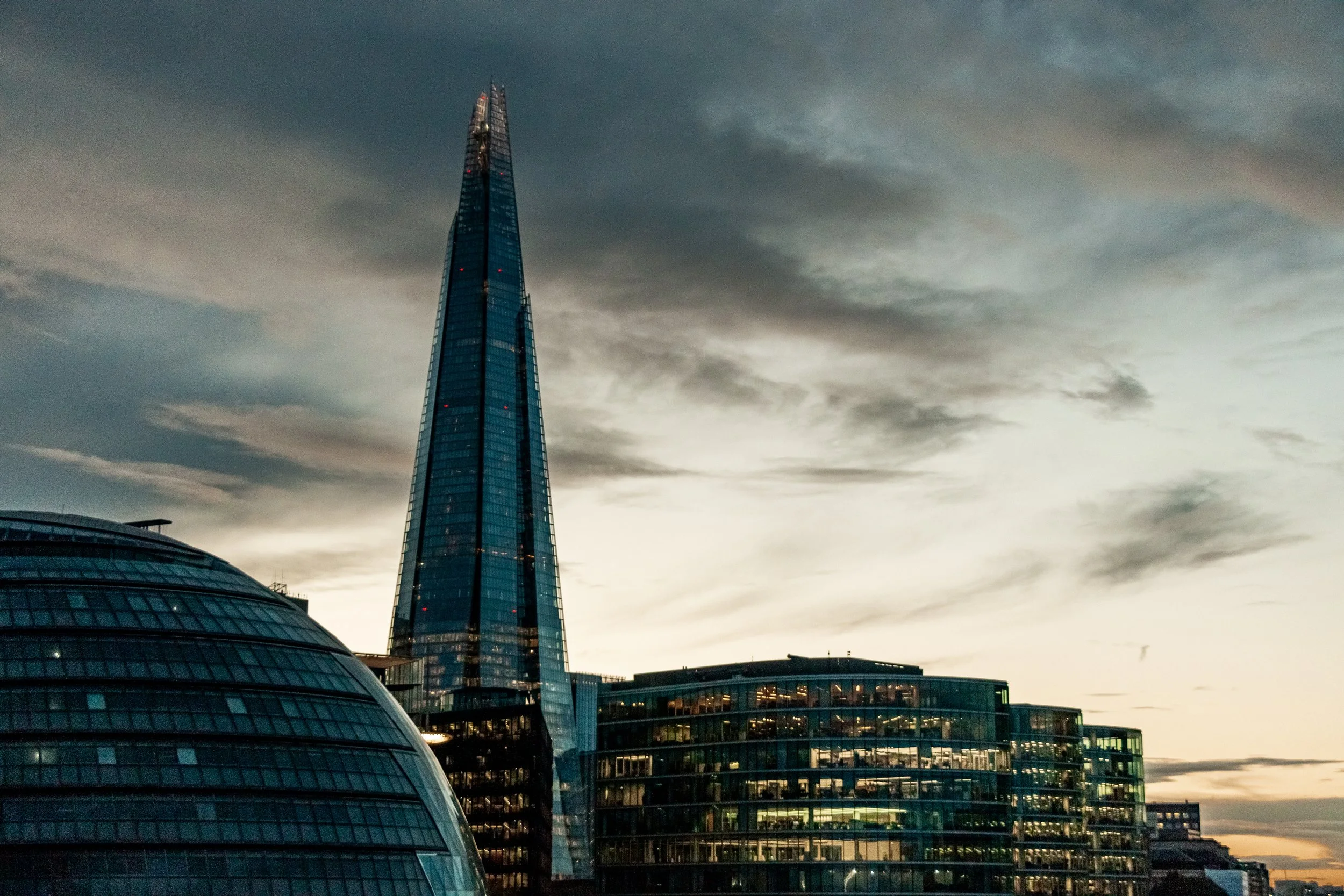 Skyline of modern skyscrapers and buildings at dusk in London, including the tall, blue-glass Shard building.