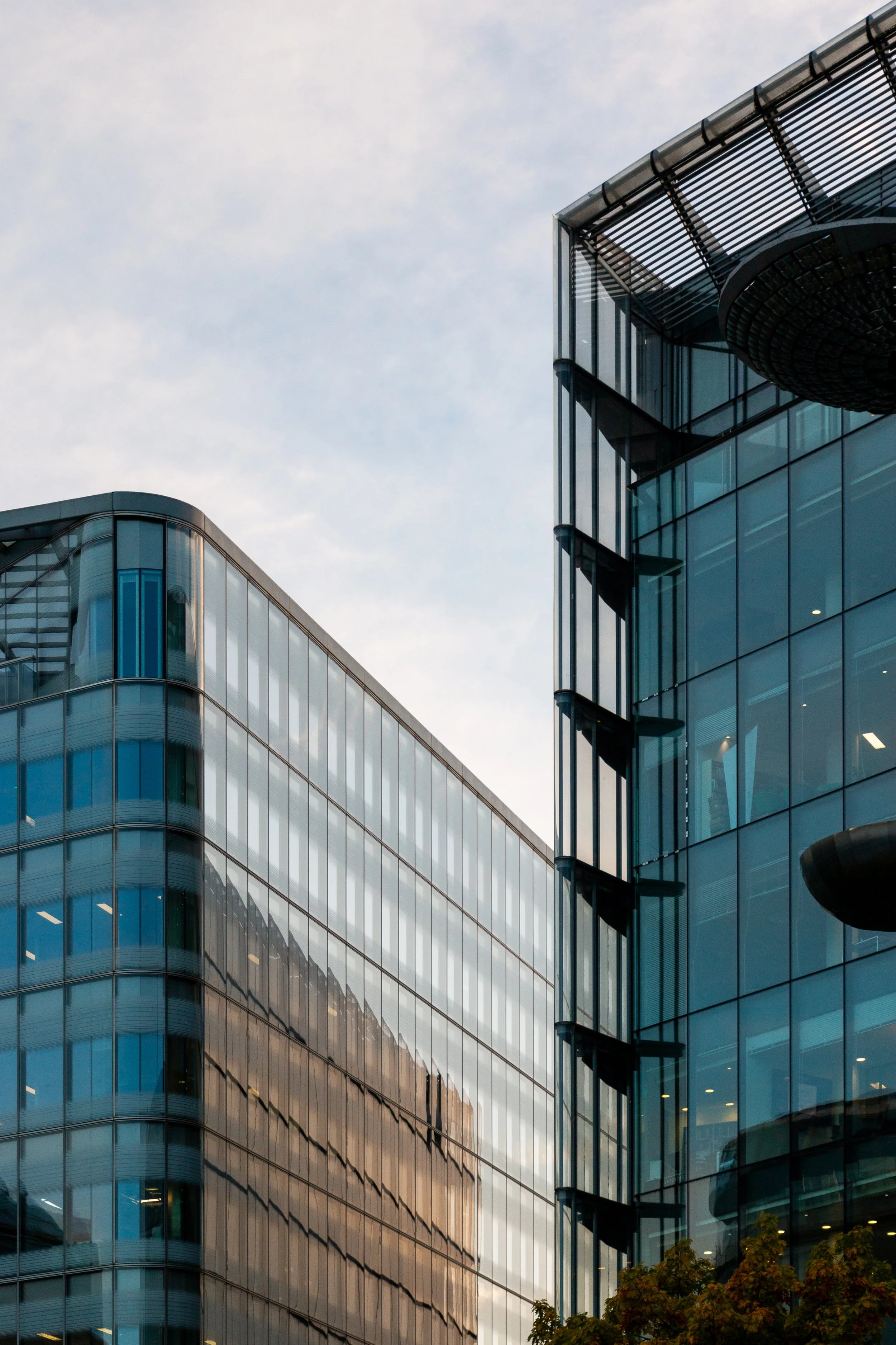 Modern glass office buildings with reflections on their facades under a cloudy sky.