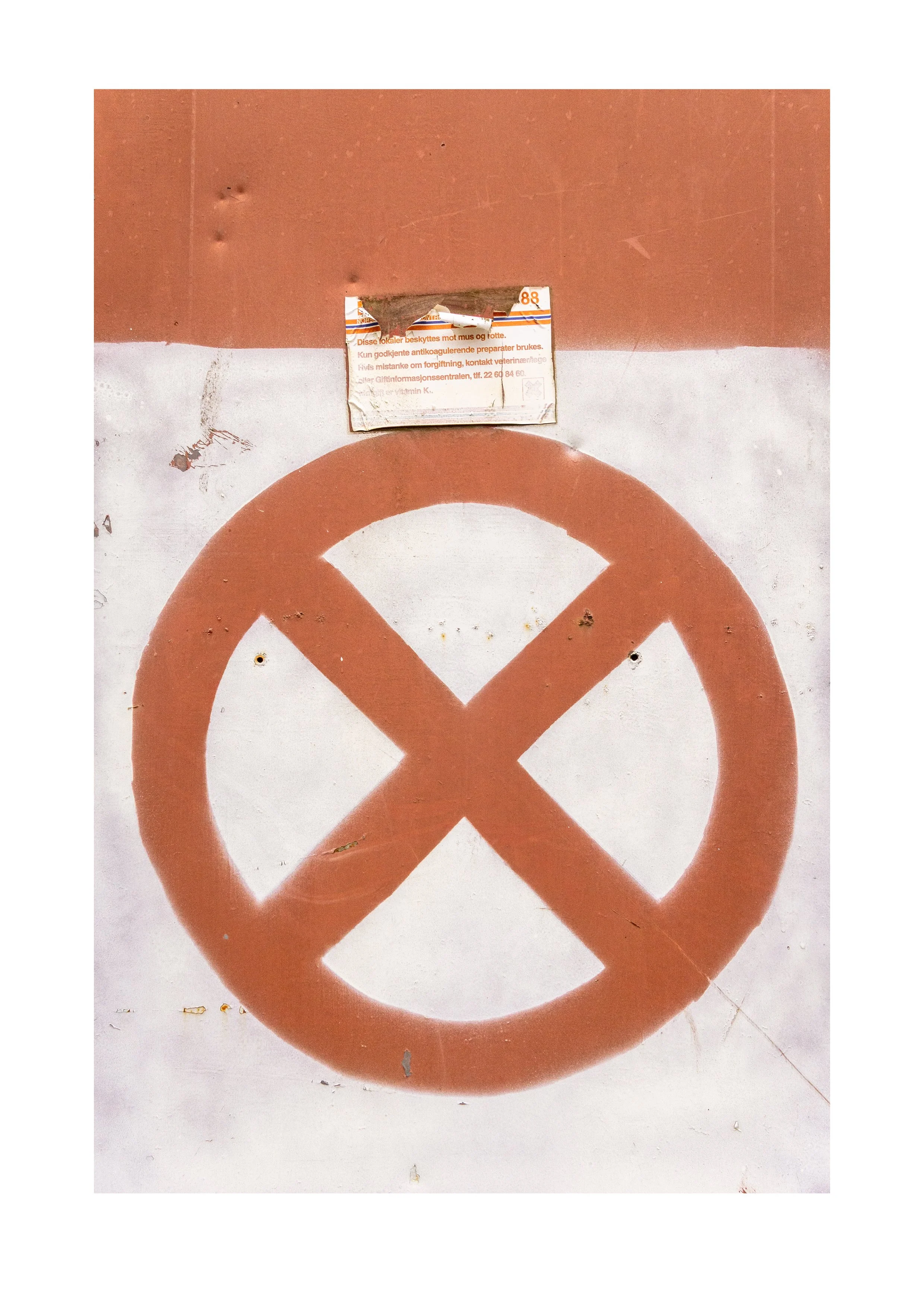 Photograph by Erik Nordby of large spray-painted prohibition symbol on a metal surface with a small weathered warning label attached above it. Archive number 000533.