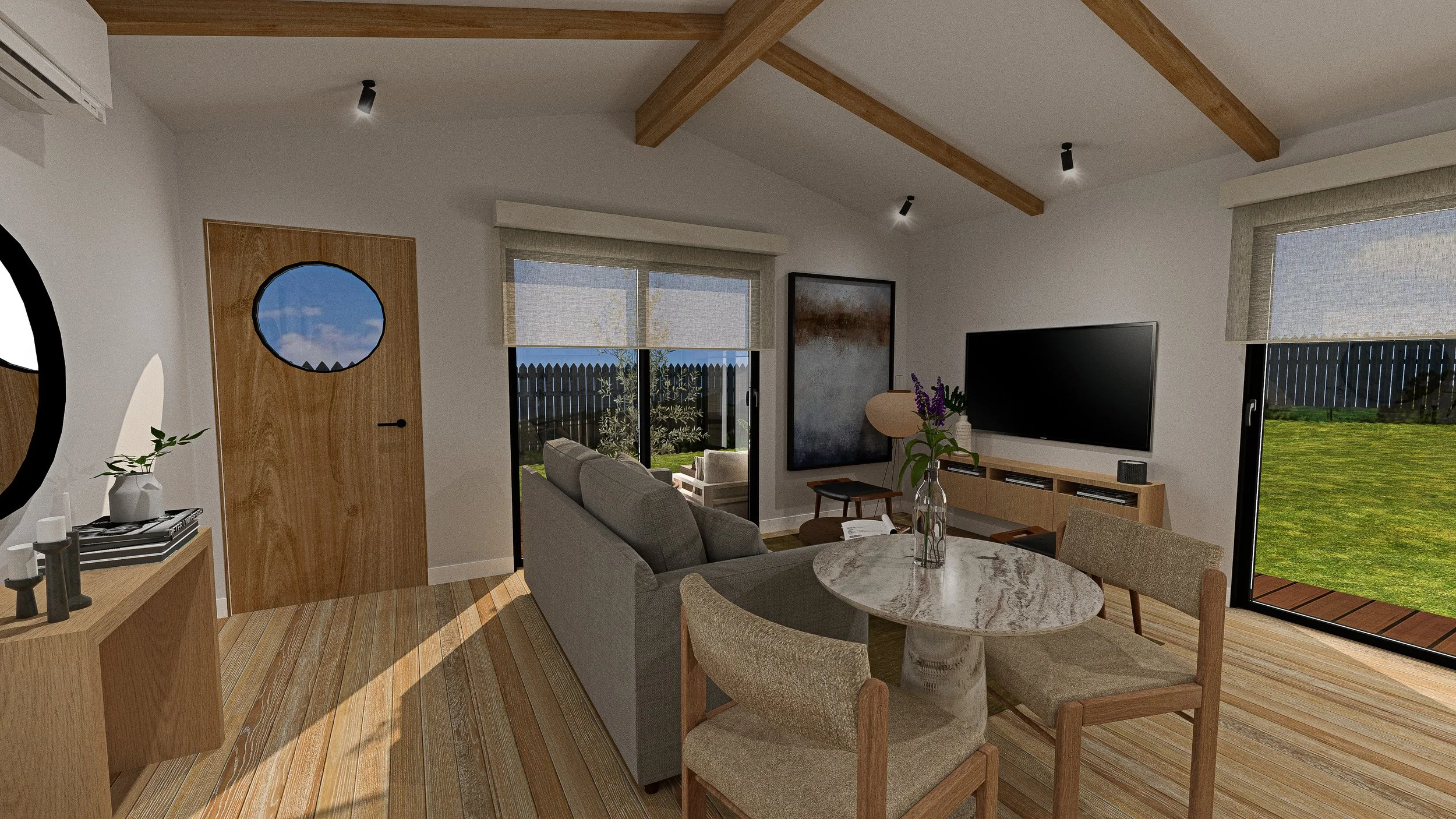 Living room with wood flooring, a gray sofa, a round marble dining table with beige chairs, a wall-mounted flat-screen TV, large sliding glass doors with outdoor view, art on walls, and natural light.