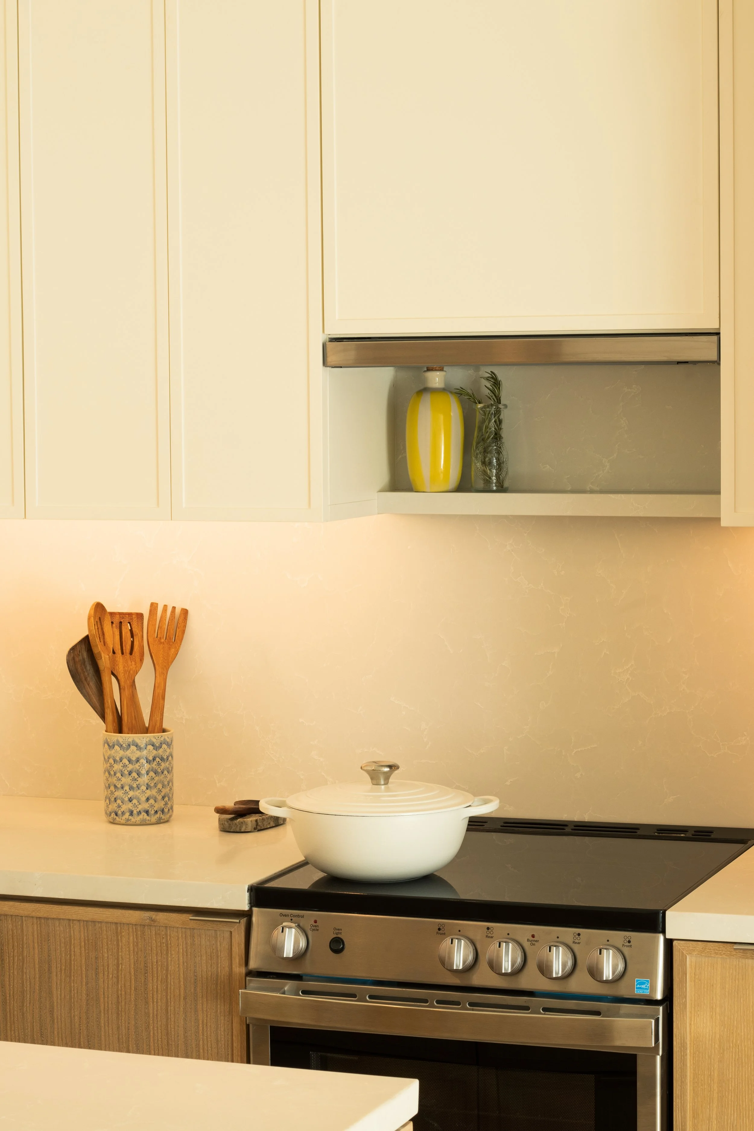 Kitchen counter with a white pot on an electric stove, a container holding wooden utensils, and a decorative vase in a kitchen with light-colored cabinets.
