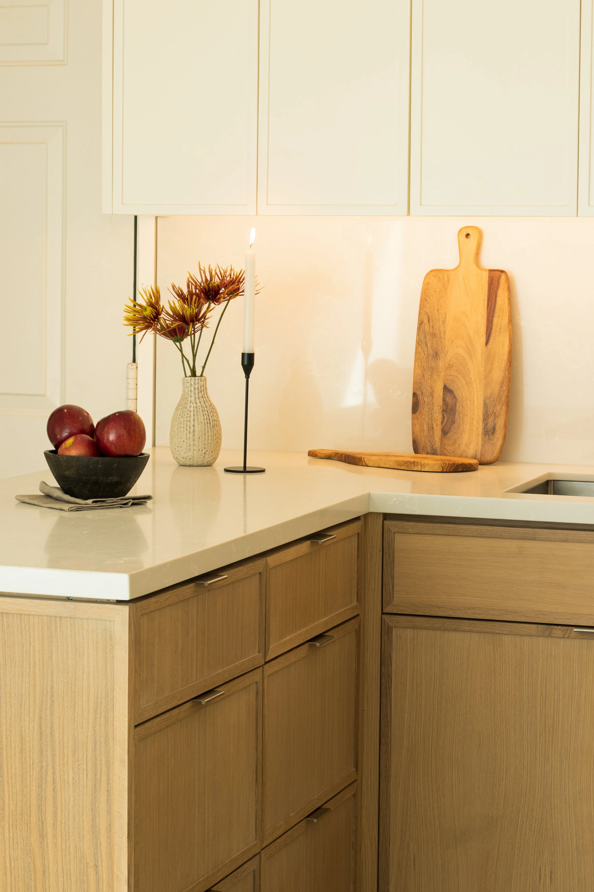 Kitchen countertop with apples in a bowl, a vase with flowers, lit candles, and wooden cutting boards.