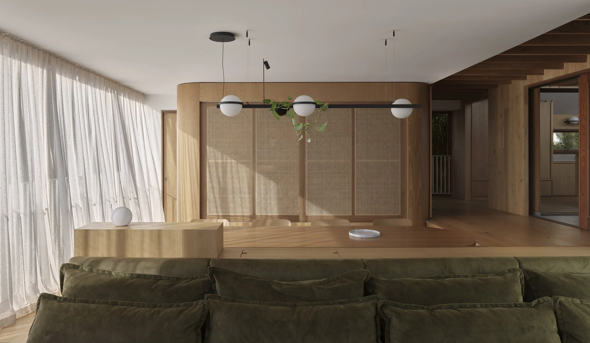 Modern living room with a large wooden dining table, green upholstered couch, white curtains, and natural wood paneling accents.