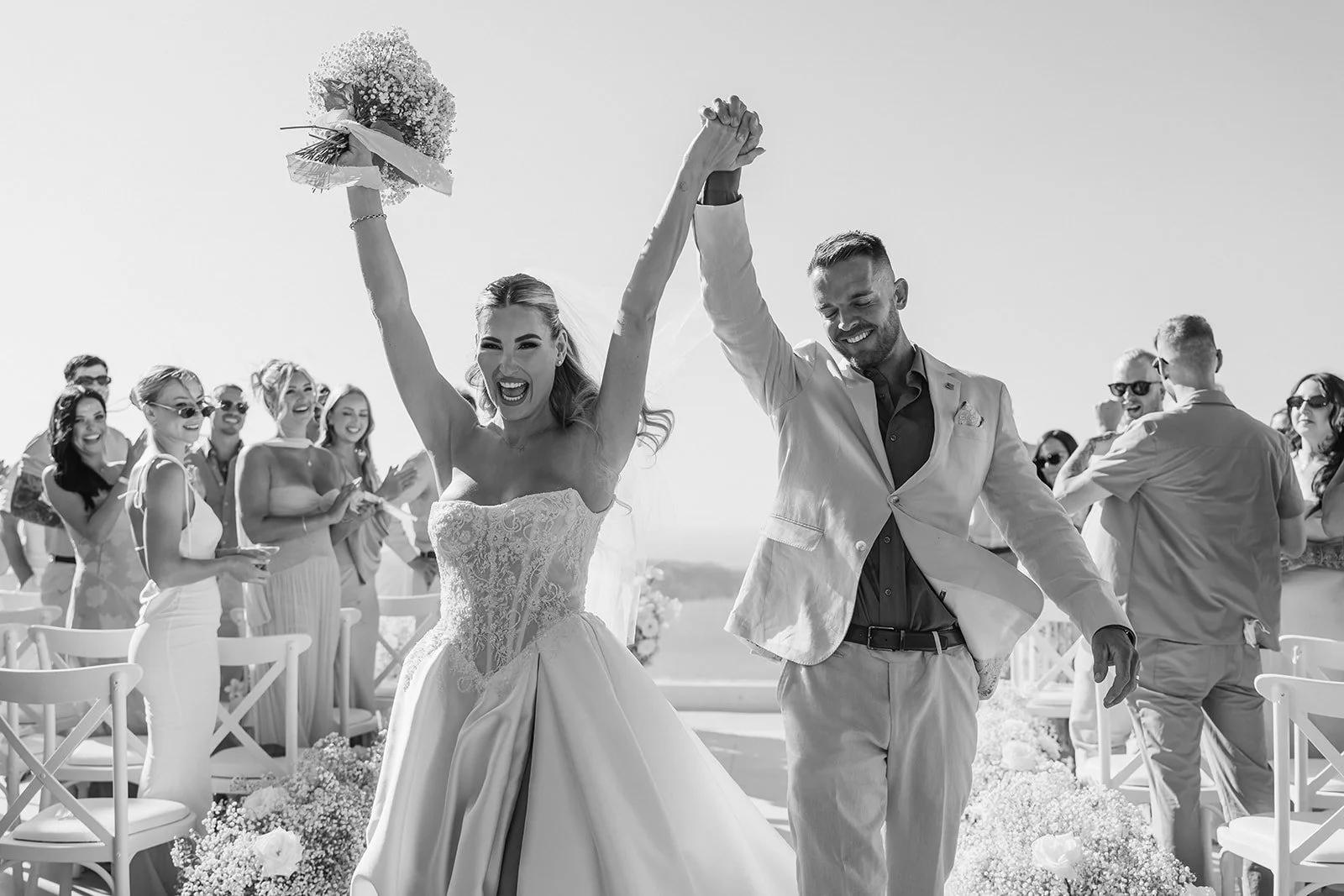 Newlyweds celebrating joyfully with raised bouquet at their luxury Santorini wedding ceremony.
