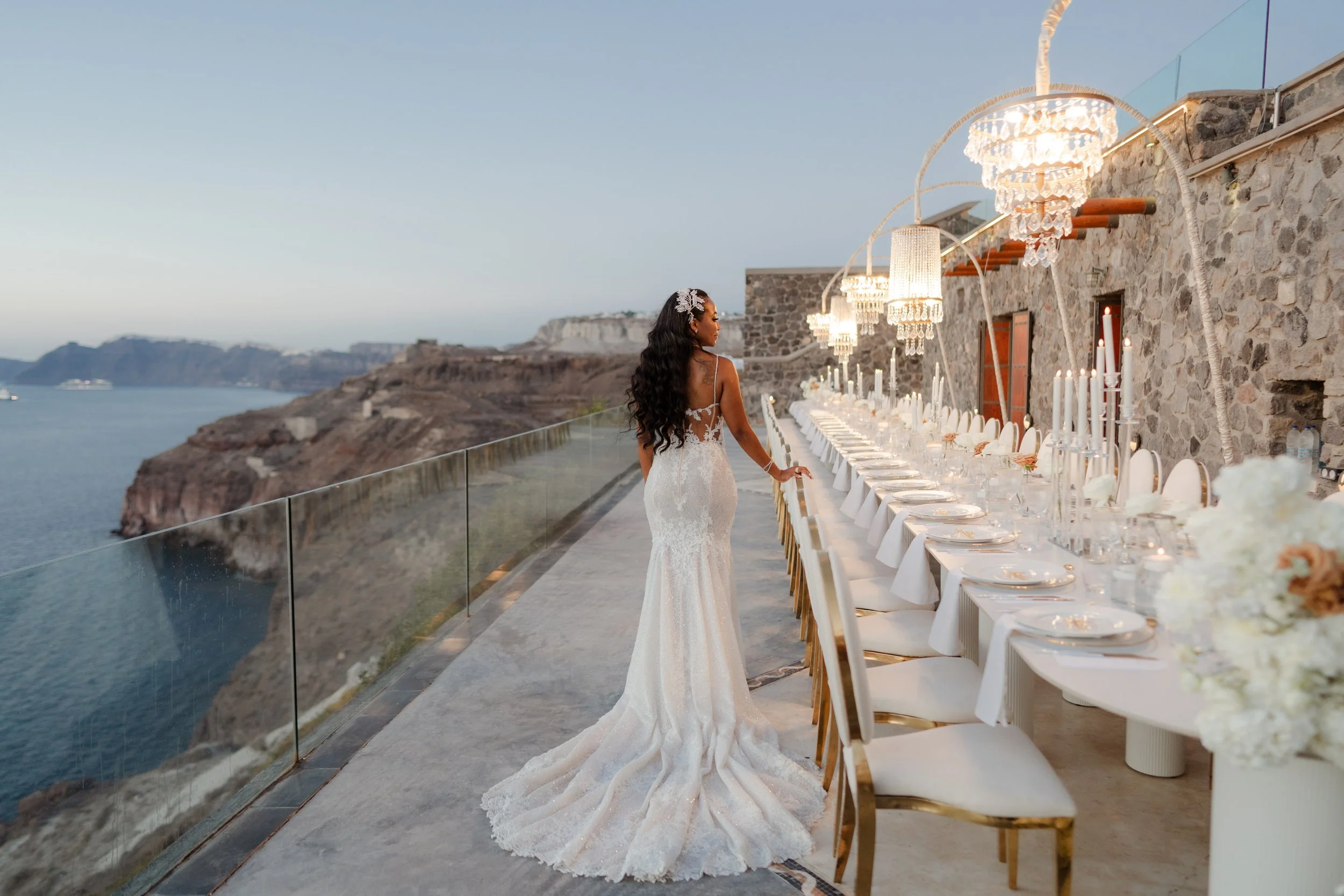 Luxury Wedding Bride in Santorini, Greece
The bride walks through a beautifully styled reception setup with chandeliers and chic table décor. A stunning moment from a luxury wedding in Greece.