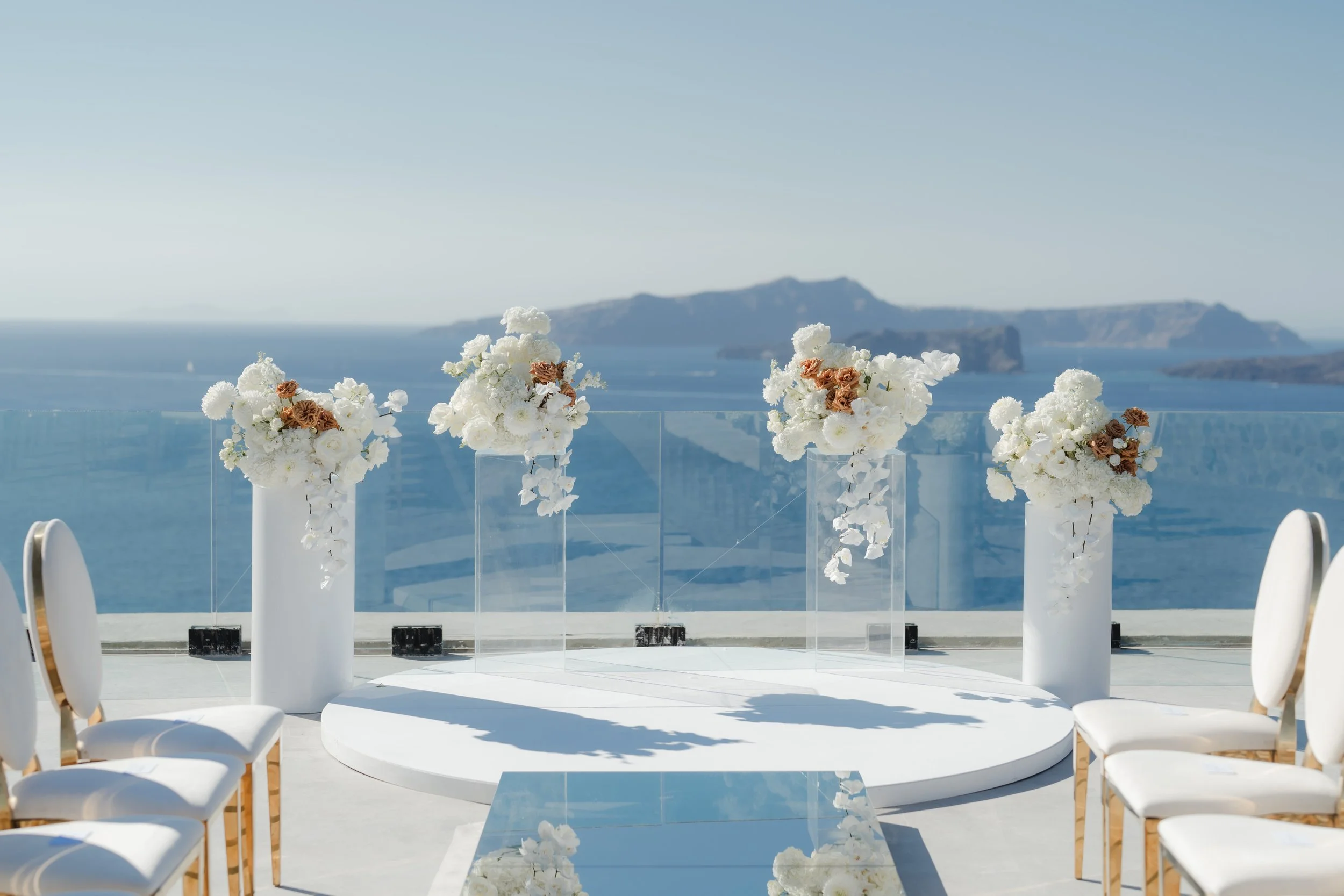 Luxury Wedding Ceremony Setup in Greece
A stunning floral arch over a glass platform with panoramic sea views. This luxury Santorini ceremony design combines sophistication, romance, and the iconic beauty of Greece.