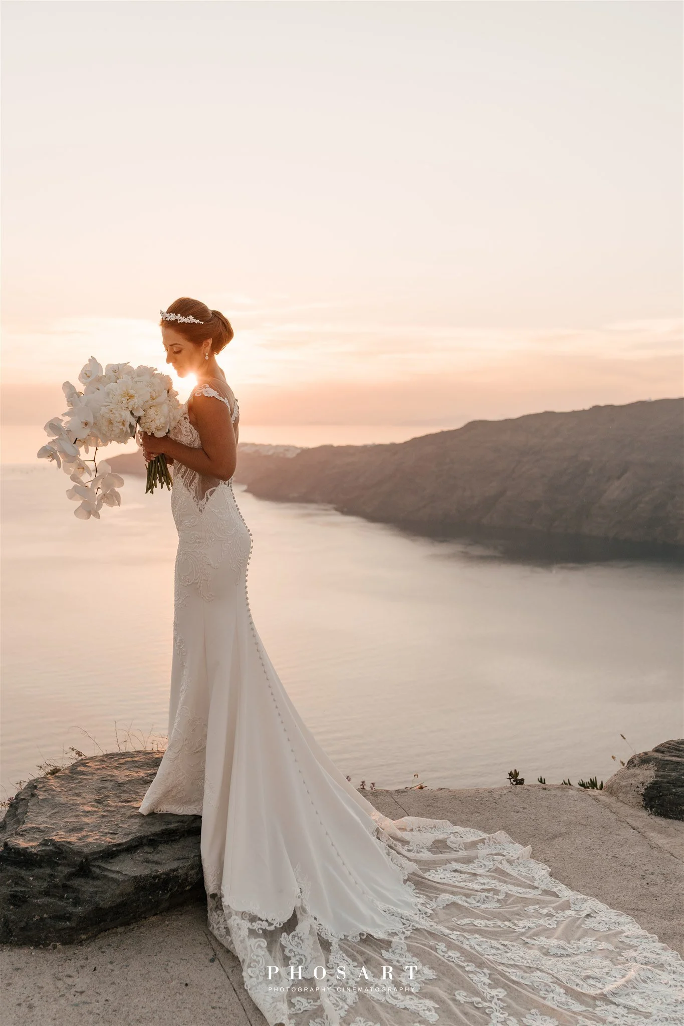 The bride in an elegant bridal look against the Santorini sunset, captured in a romantic photoshoot moment.