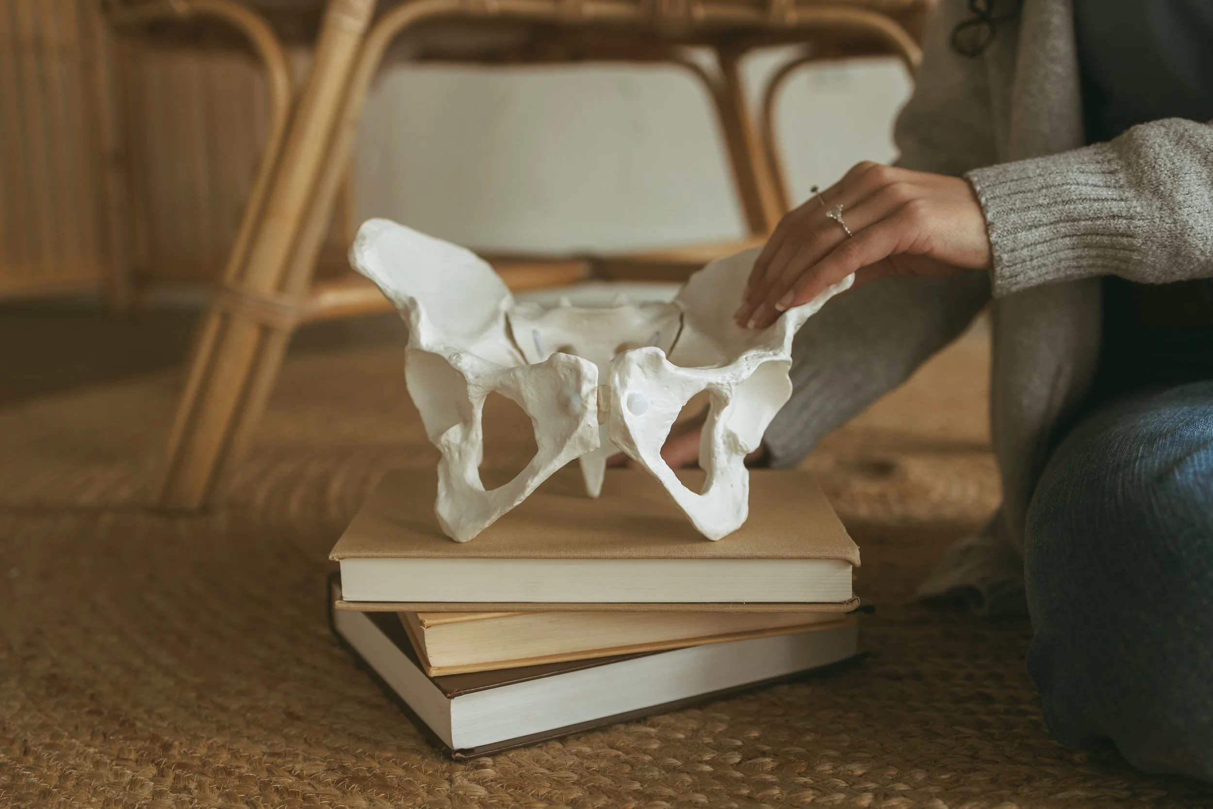 Person placing a plaster cast of a human pelvis on top of stacked books on a woven floor mat.