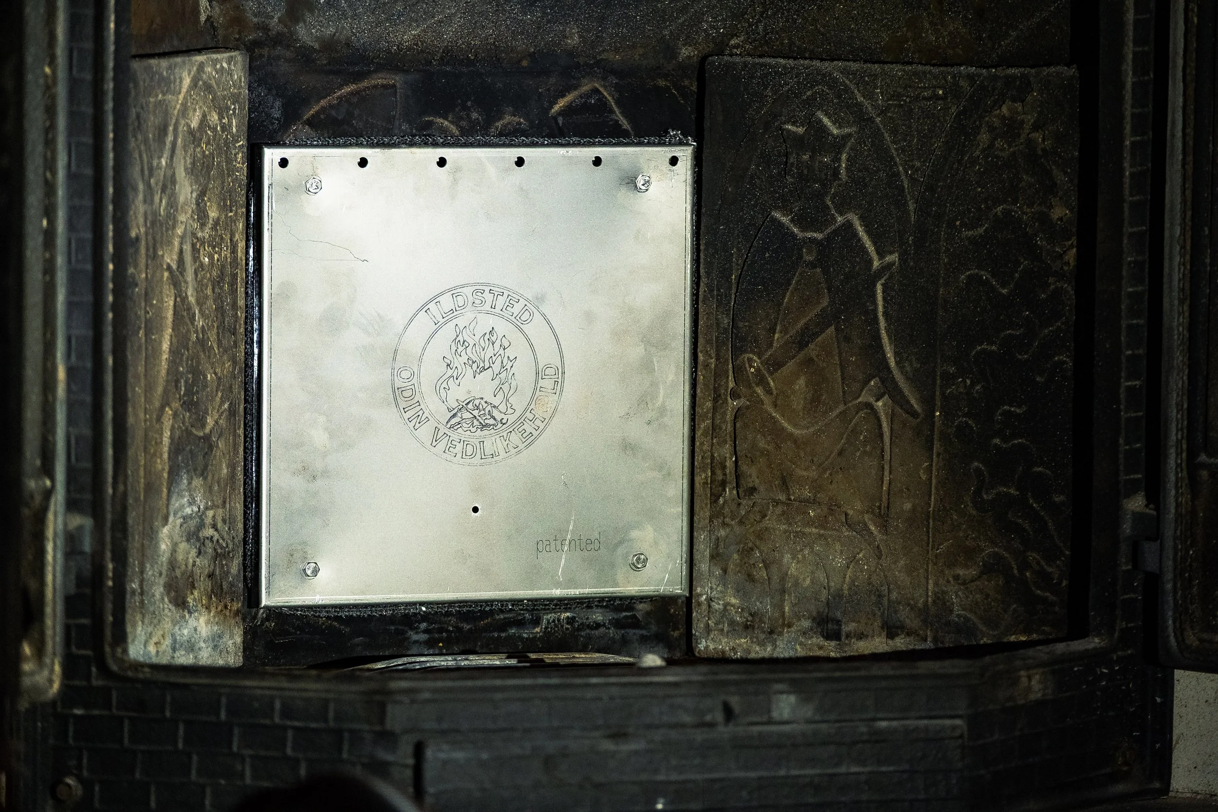 Et ildsted med en metallplate som har en logo og teksten "ILDSTED ODIN VEDLIKEHOLD".
