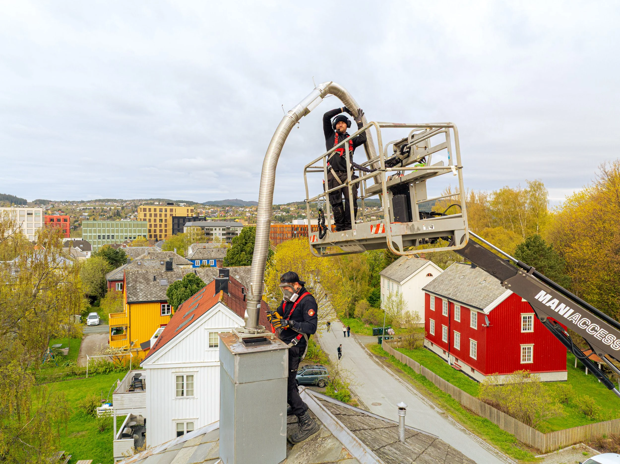 To mestere jobber på taket av en bolig og jobber med vedlikehold av skorstein.