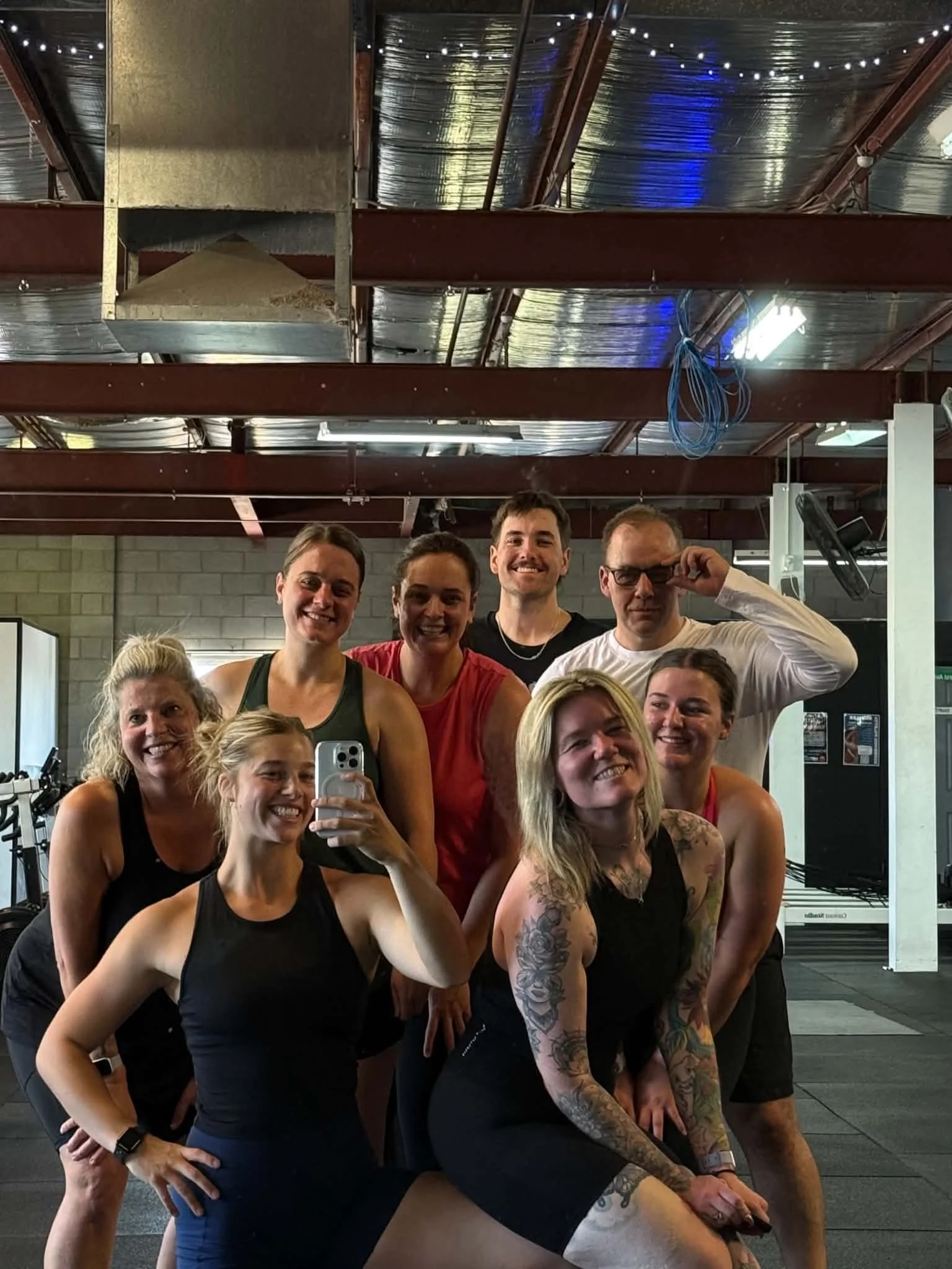 Group of people in workout attire posing together in a gym, smiling for a mirror selfie.
