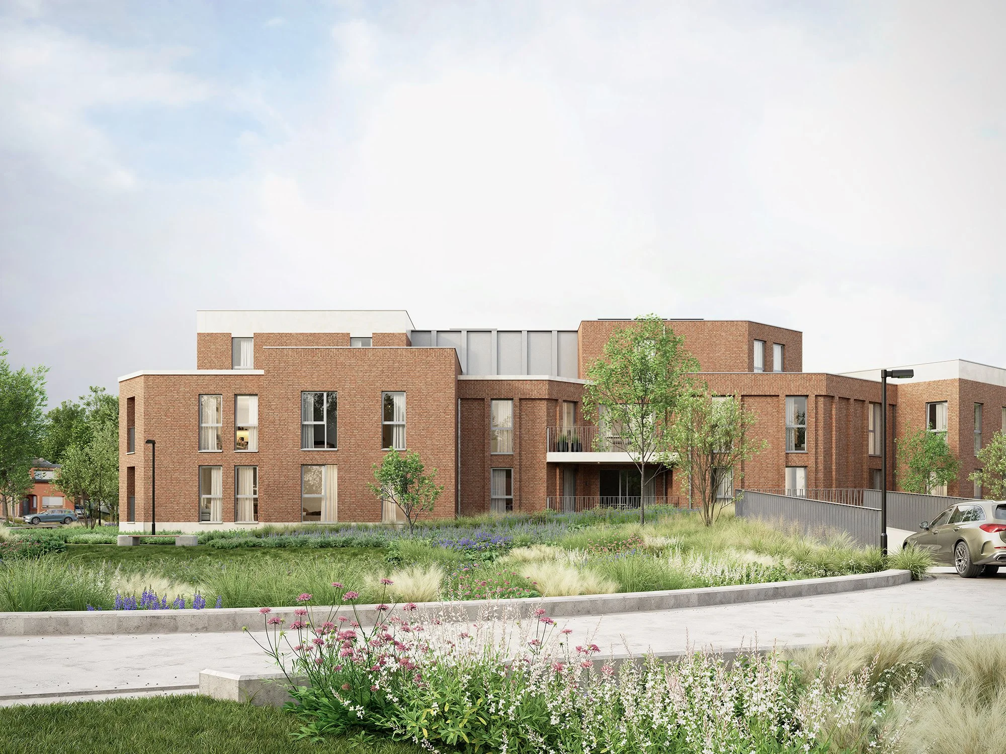 Moderne rood bakstenen appartementsgebouw met bomen en bloemrijke tuinen op voorgrond, parkeerplaatsen en straatlantaarn, onder een heldere hemel.