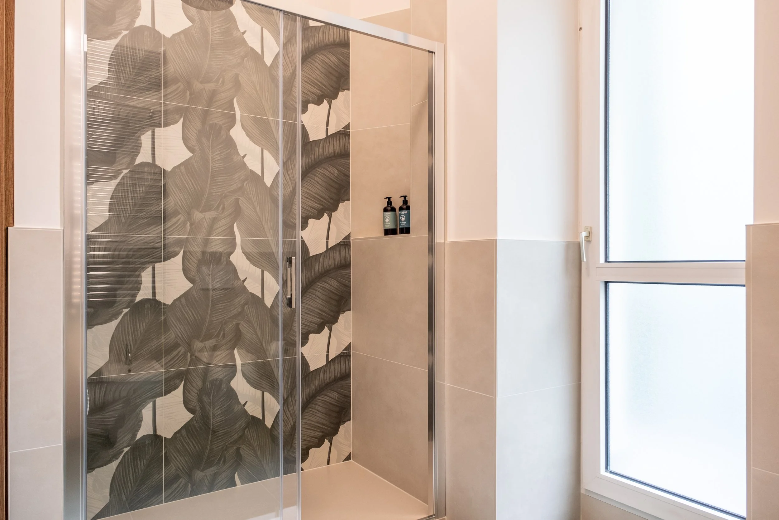 Doccia con parete decorata con piastrelle a motivo di grandi foglie di piante tropicali
