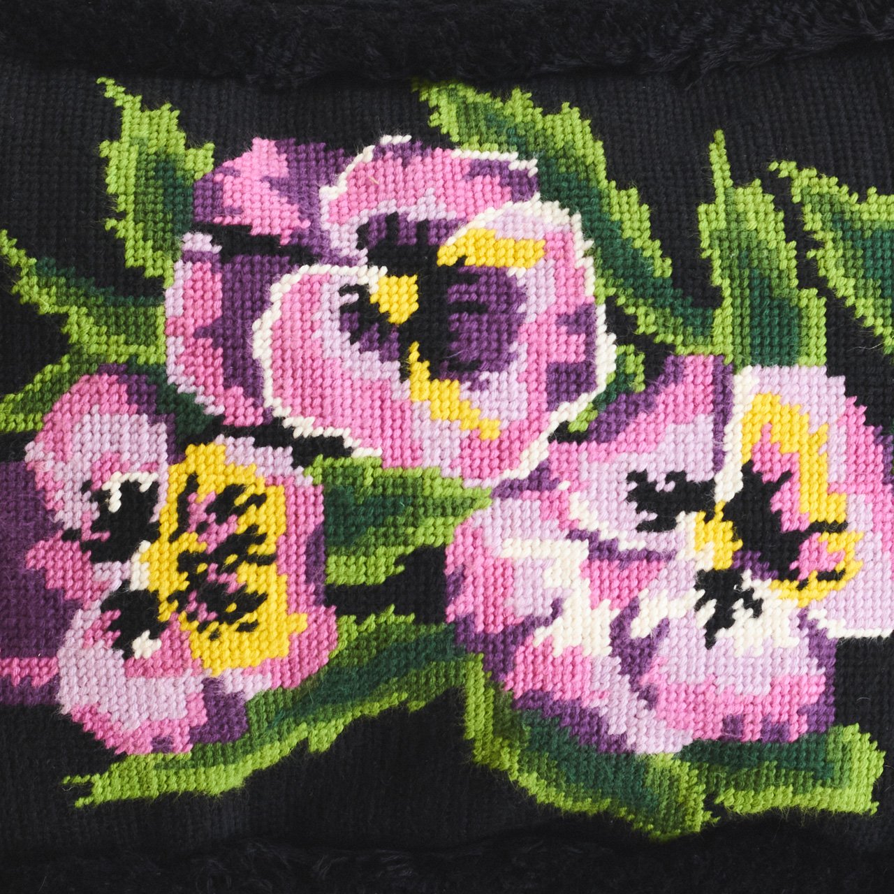 Cross-stitch embroidery of pink and yellow roses with green leaves on black fabric.