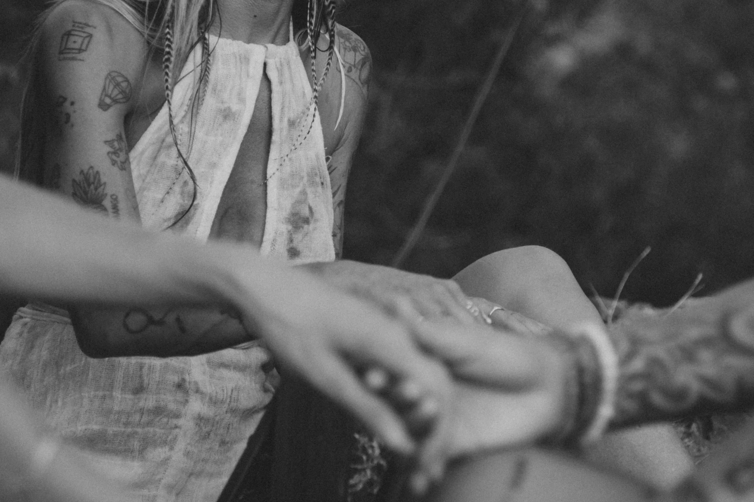 Close-up of a person with tattoos, wearing a sleeveless top, touching another person's arm during the daytime.