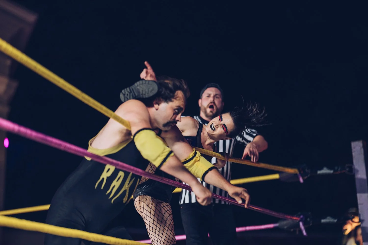 Wrestling match with a man and woman fighting inside a ring, with a referee watching
