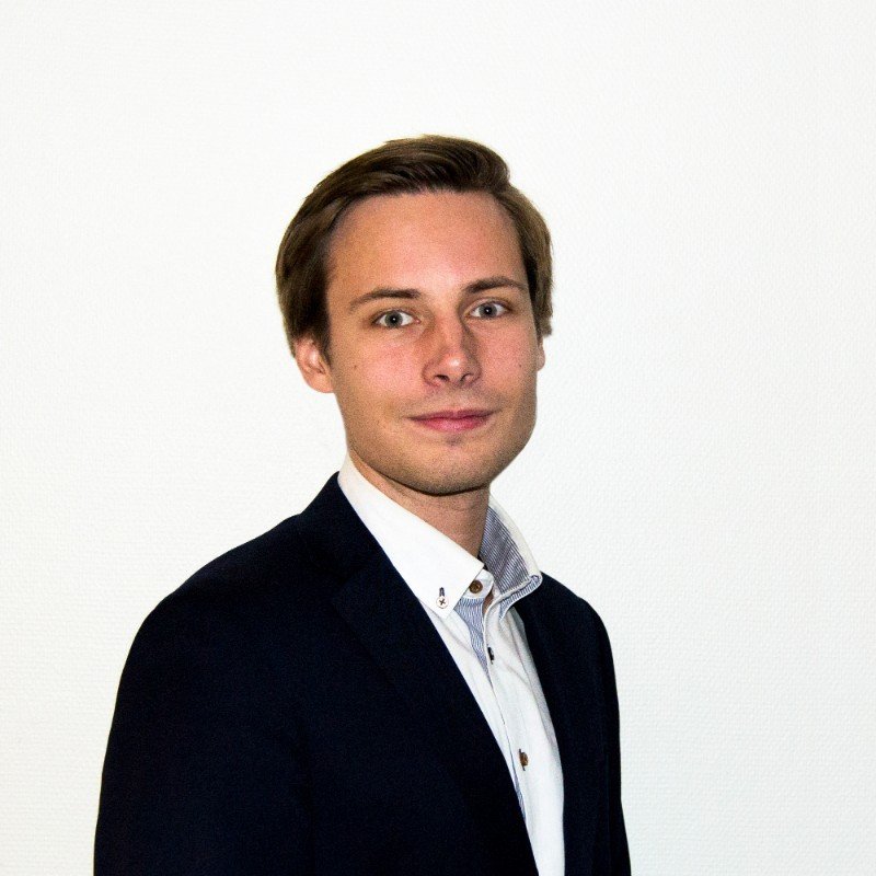 A young woman with brown hair and blue eyes wearing a black and white striped shirt, outdoors at sunset with a blurred dark landscape in the background.