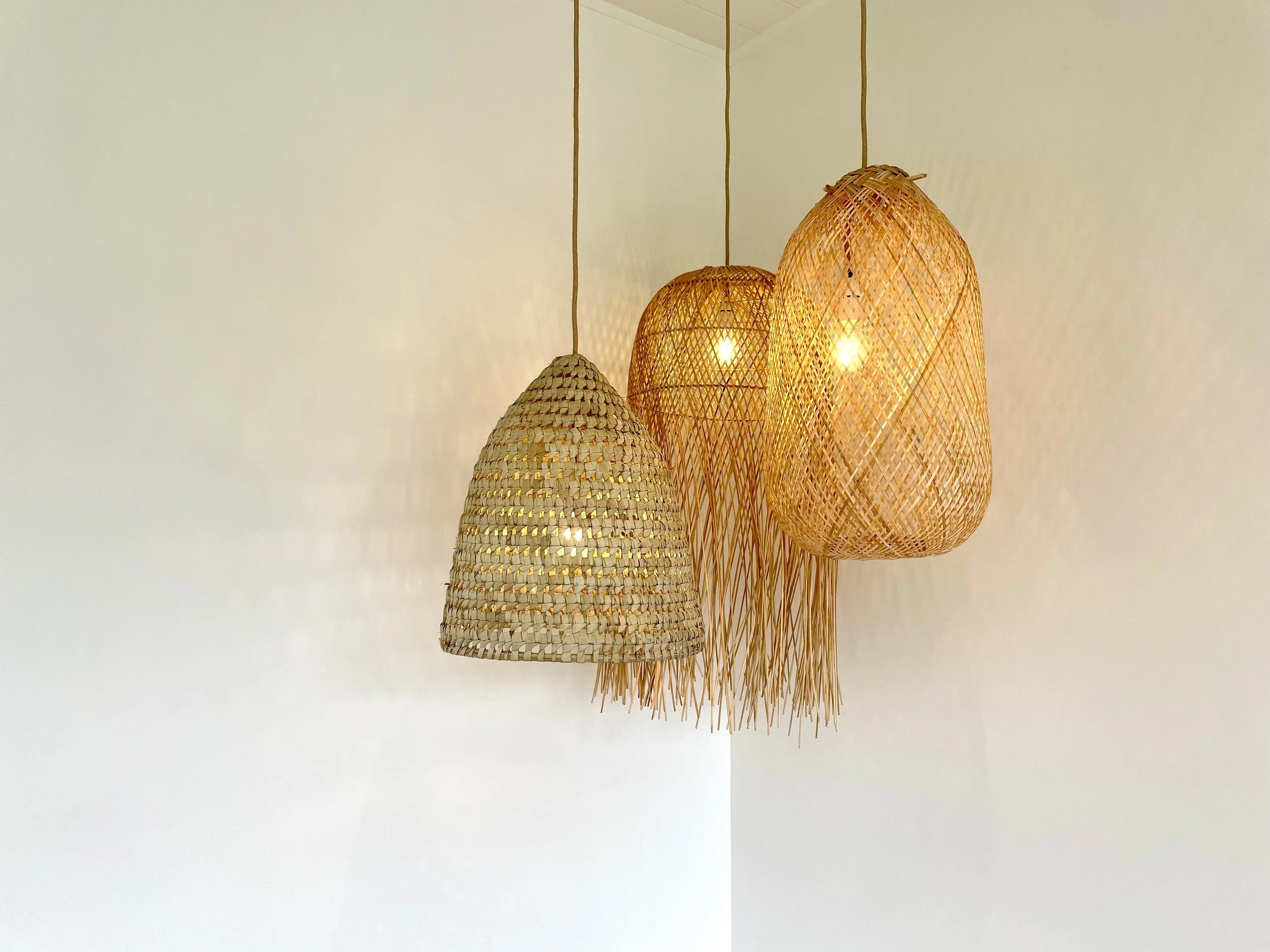 Three hanging woven rattan pendant lights on a white wall, illuminated and casting shadows.